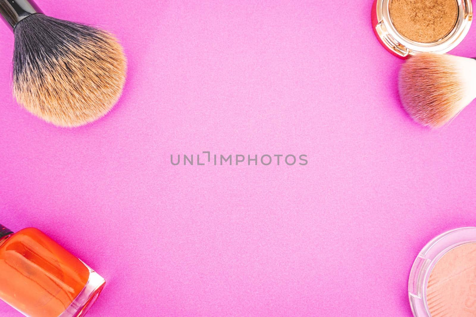 Flatlay of make up and beauty products on a pink background.