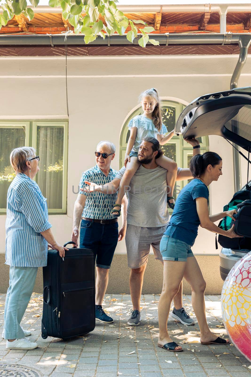 Relaxed people leaving on summer journey, putting travel bags and inflatable in automobile trunk. European family travelling together on vacation journey, loading luggage and suitcase.