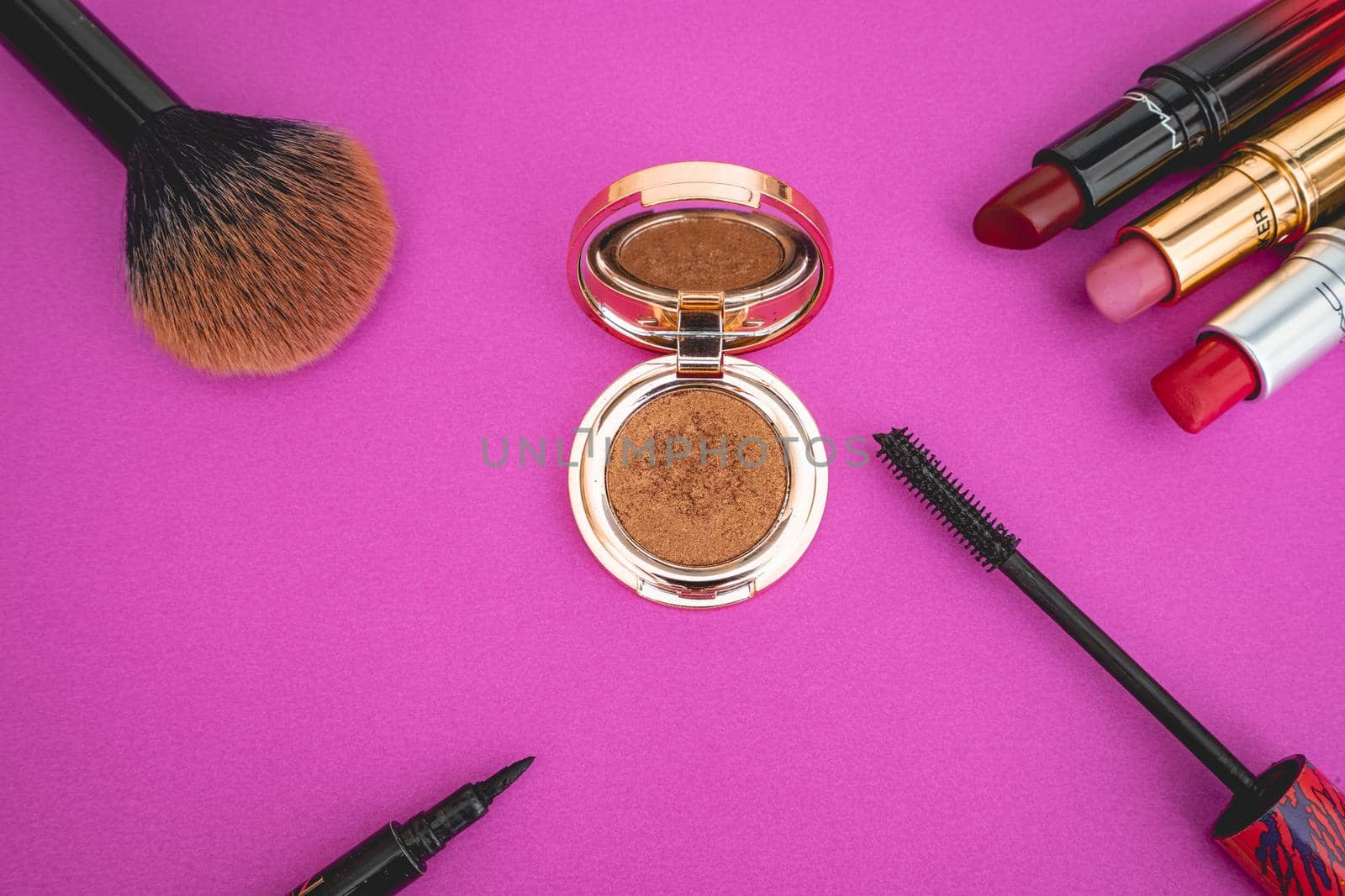 Flatlay of make up and beauty products on a pink background.