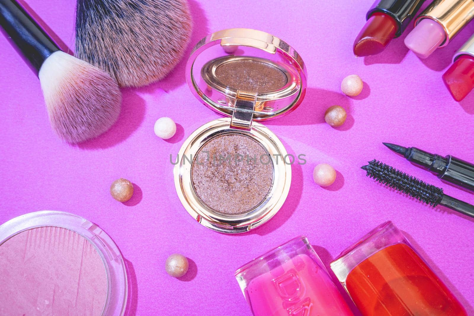 Flatlay of make up and beauty products on a pink background.