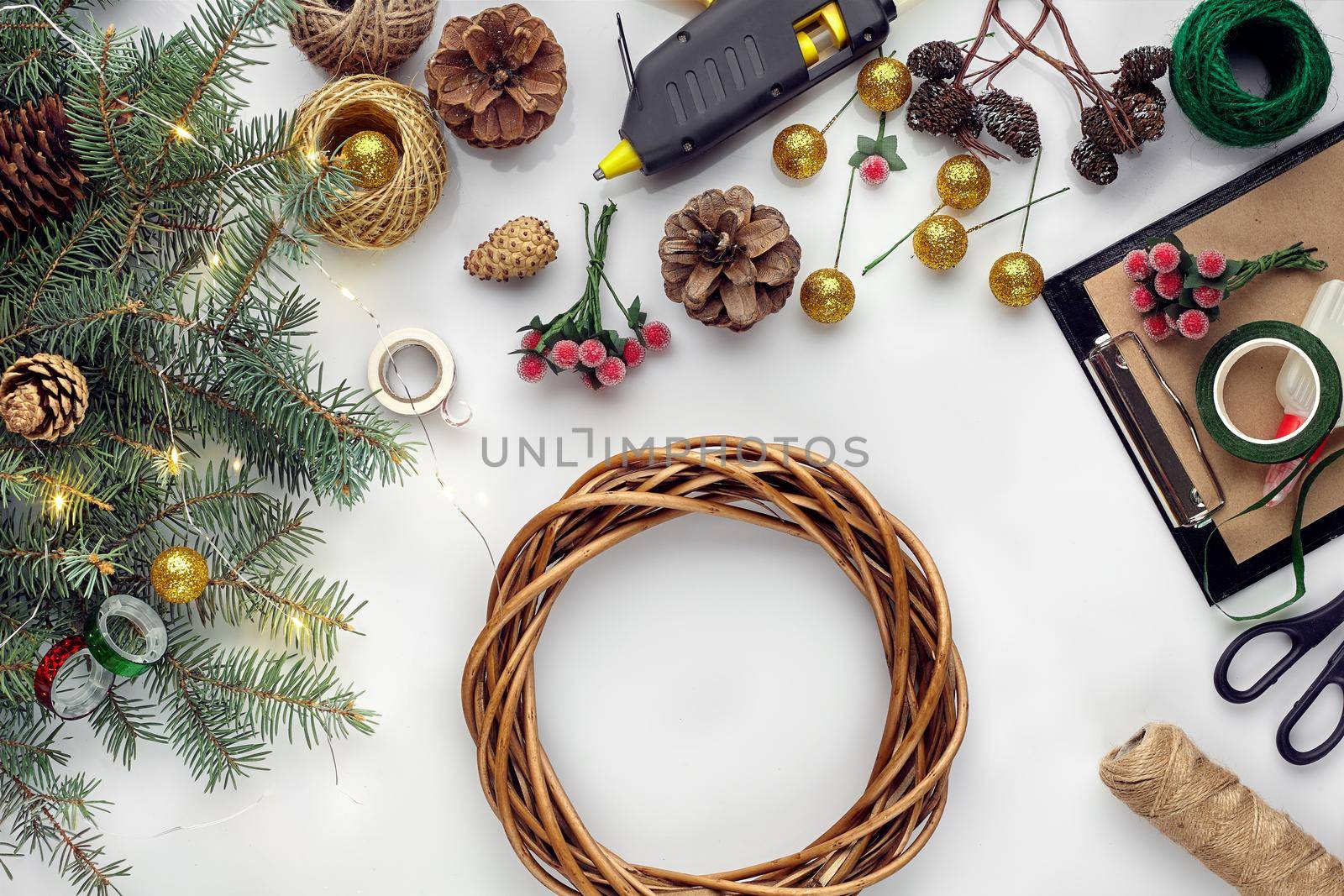Preparing for Christmas or New Year holiday. Flat-lay of fur tree branches, wreaths, rope, scissors, craft paper over white table background, top view, copy space, horizontal composition