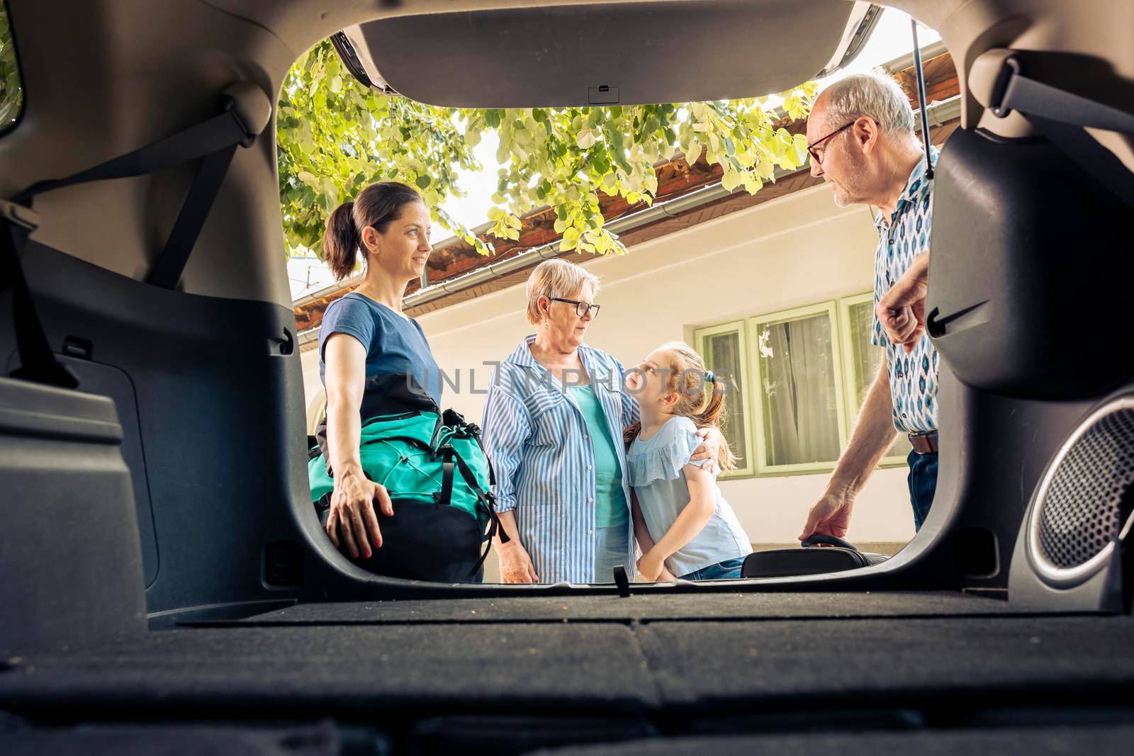 European family going on summer holiday with luggage and bags, loading baggage in automobile trunk. Little girl with mother and grandparents travelling on vacation trip with vehicle.