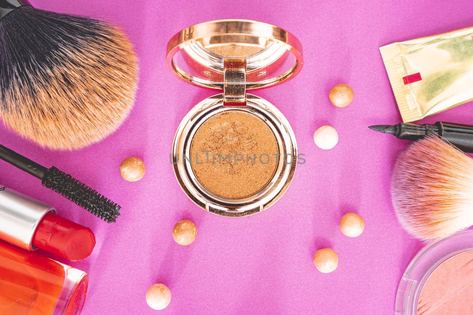 Flatlay of make up and beauty products on a pink background.