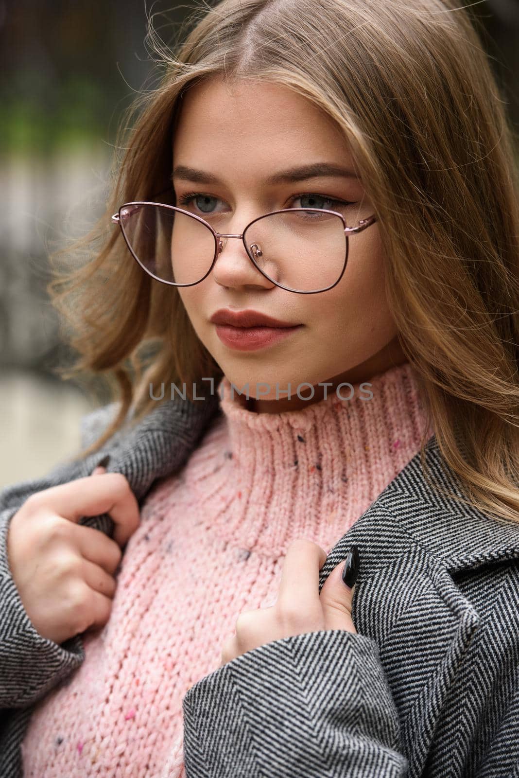 young beautiful girl posing on the street. Dressed in a stylish gray coat, knitted pink sweater and skirt.