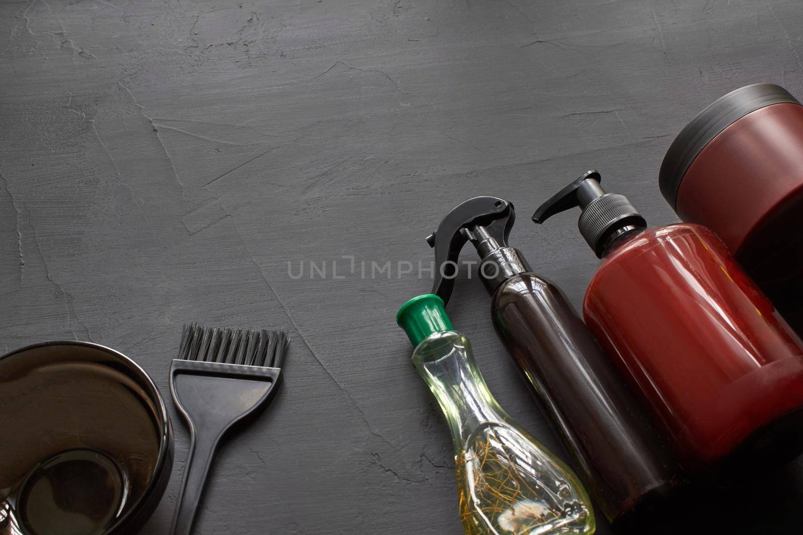 Branding mockup of a professional haircutter kit with copy space on a black background. Coloring brush, plastic bowl and barbers hair care products. Top view.