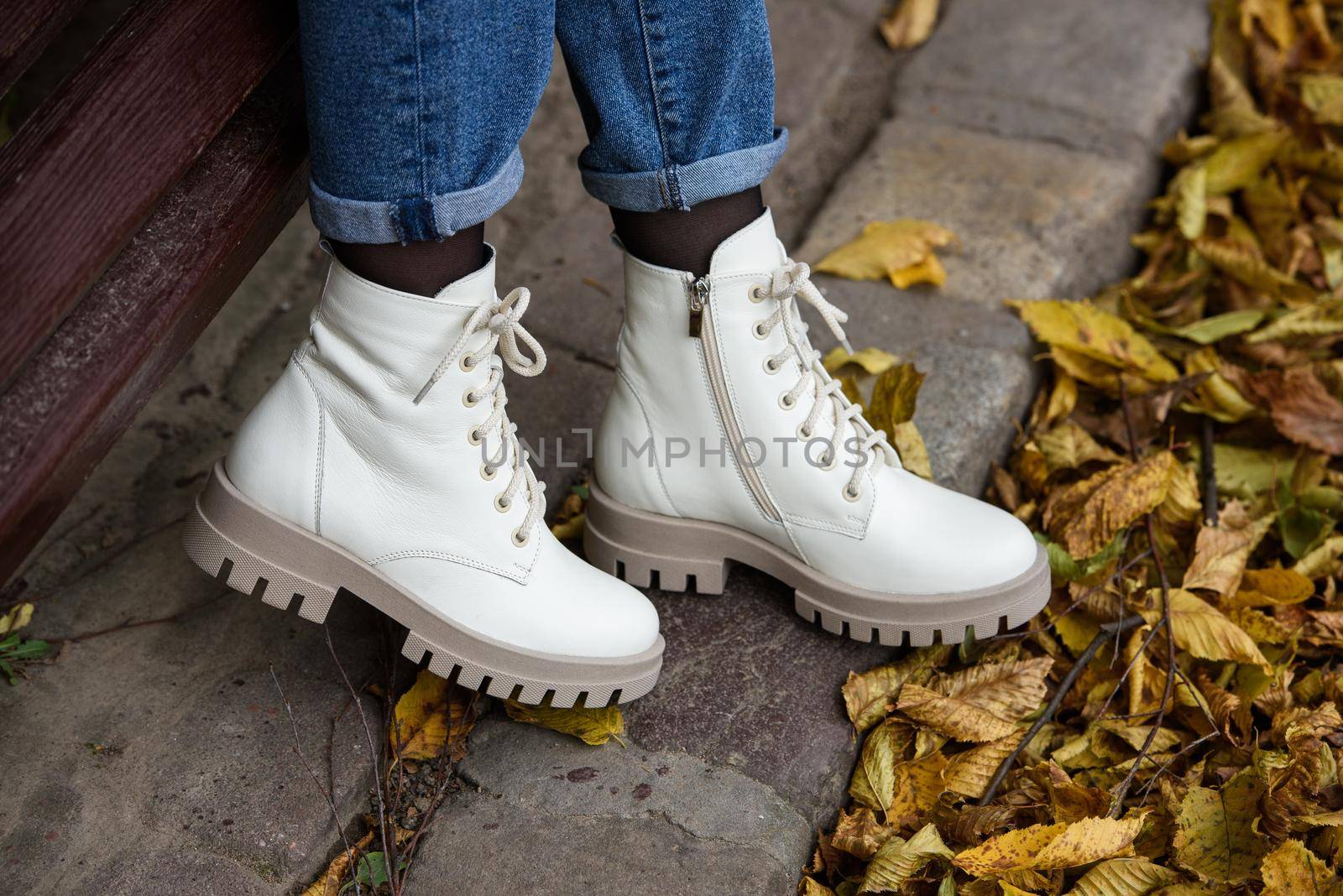 Female legs in a jeans and white fashion boots with laces. fallen leaves on the sidewalk