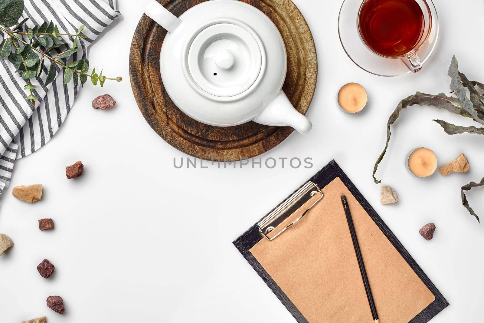 White background on which craft paper, notebook, cup with tea and white porcelain teapot. Romantic breakfast. Top view. Copy space. Still life. Flat lay