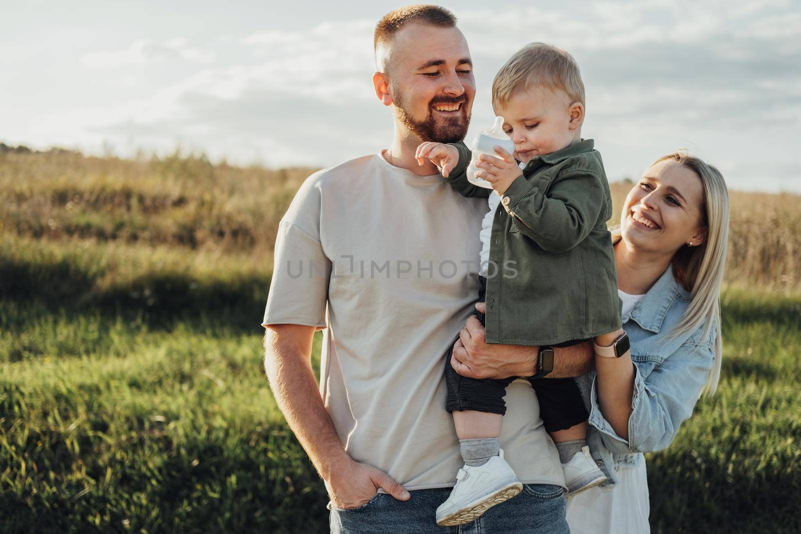 Portrait of Happy Young Family Outdoors, Father and Mother with Toddler Son Having Fun Time