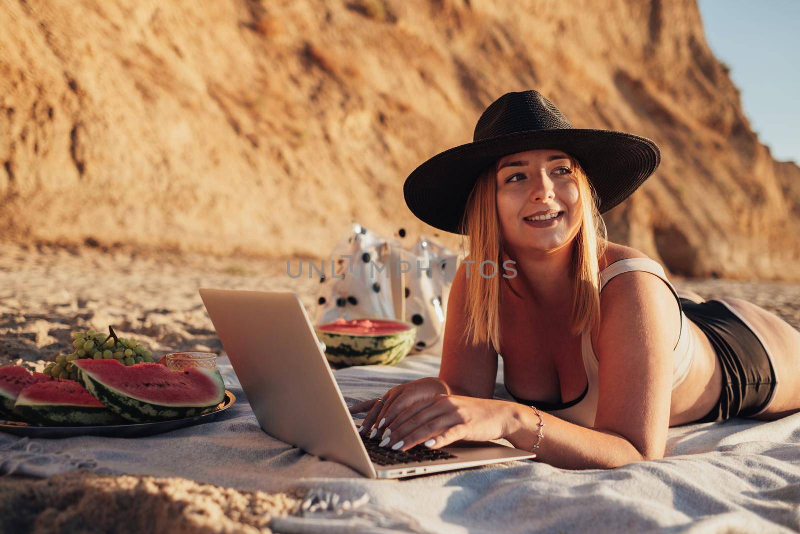Pretty Young Woman in Swimsuit and Hat Looking Away While Using Laptop on Vacation by the Sea by Romvy