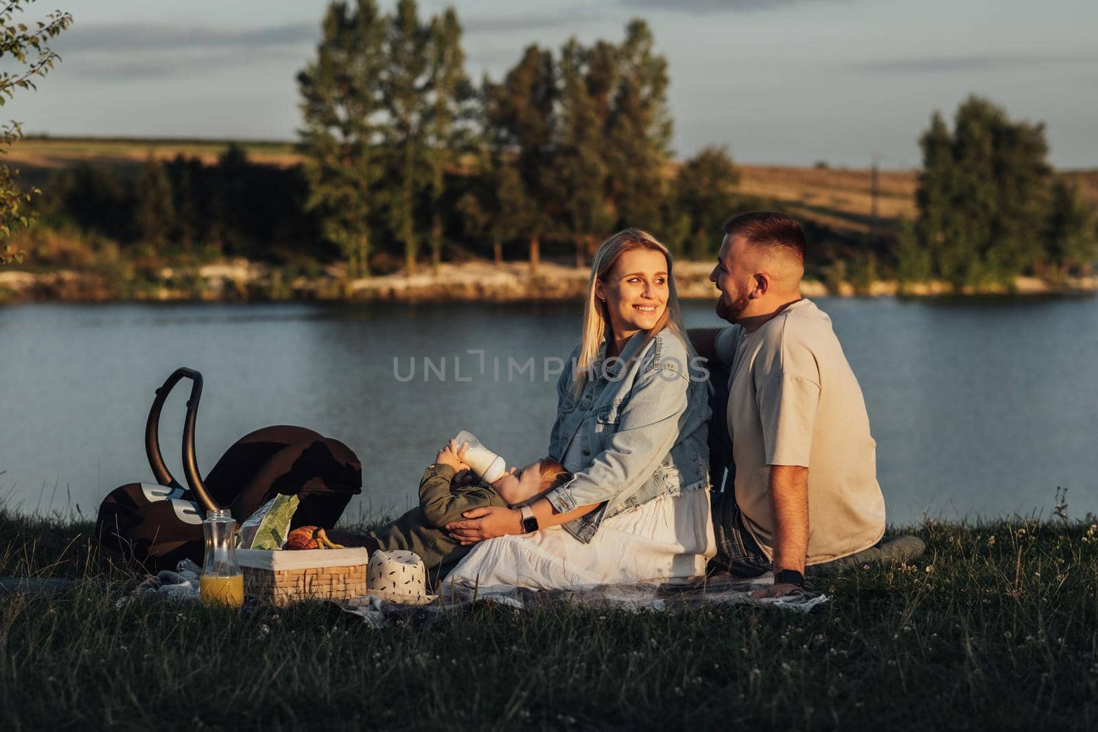 Couple with Their Little Son Having Picnic Outdoors by the Lake, Young Family Enjoying Weekend Together
