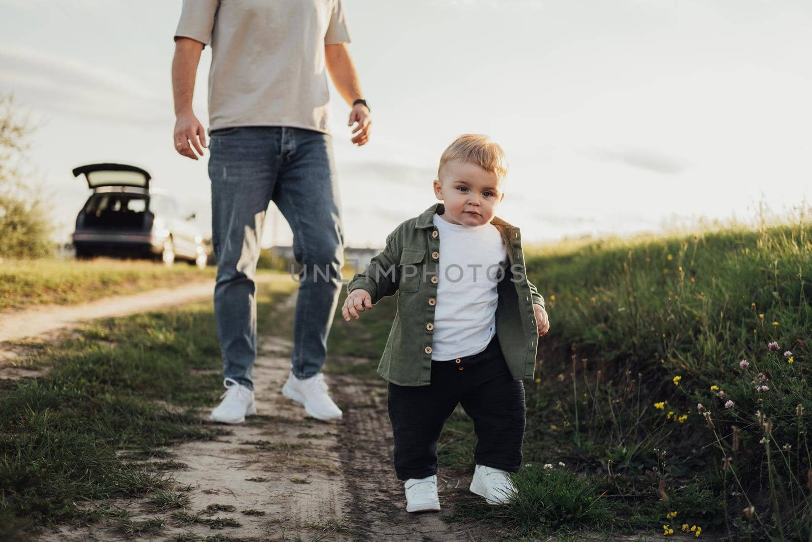 Funny Toddler Boy Trying to Walk Without Help from His Father Outdoors on Country Road