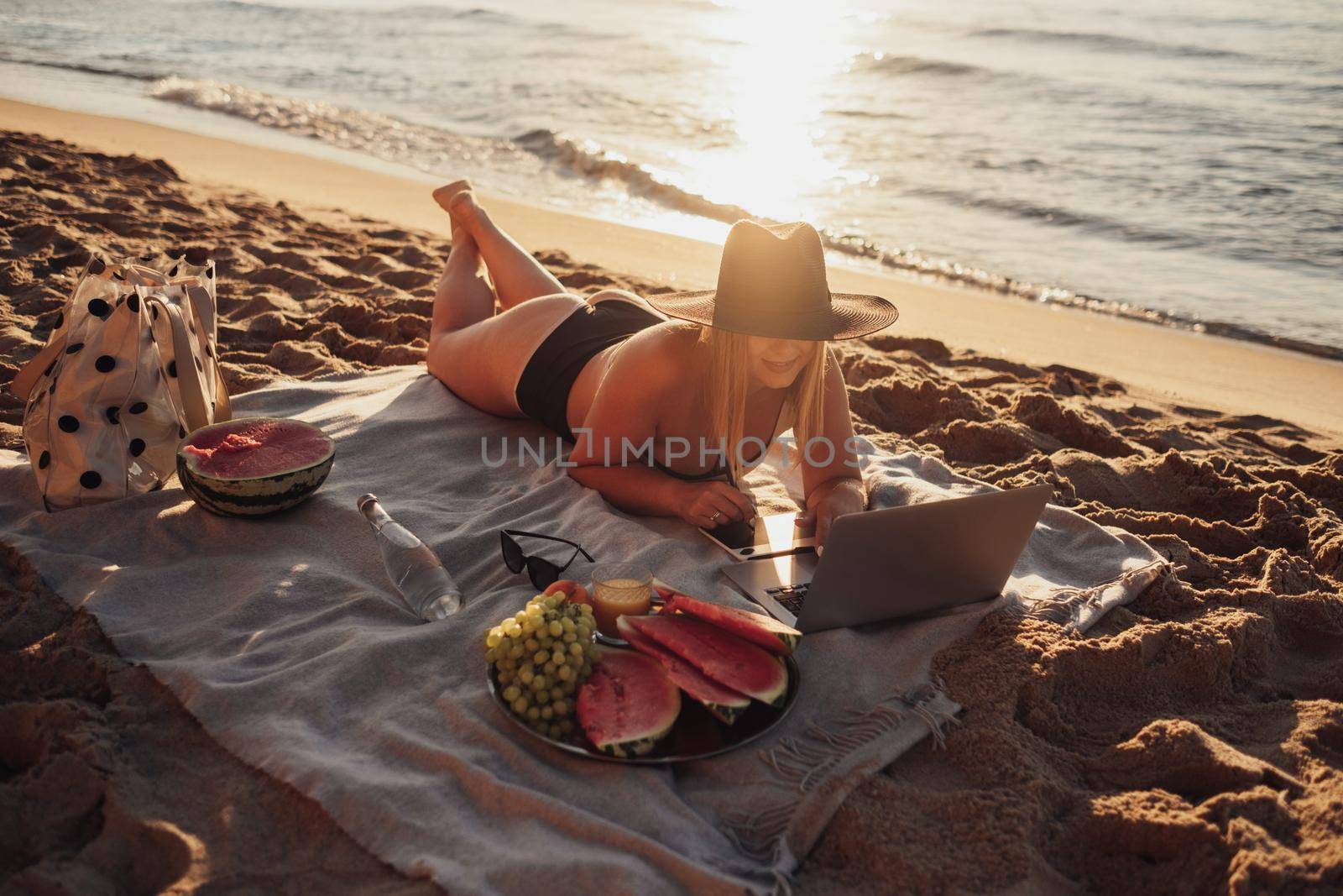 Young Woman Dressed in Swimsuit Working on Digital Tablet and Laptop During Picnic by the Sea at Sunrise, Freelance Concept by Romvy