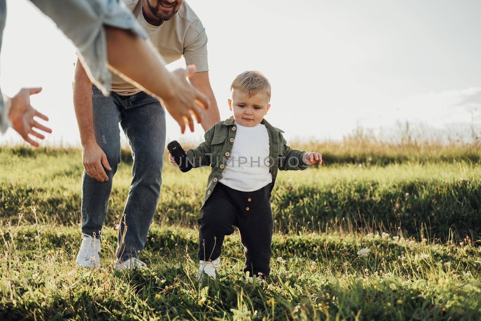 Father and Mother Help Their Toddler Son Take First Steps, Family Weekend Outdoors