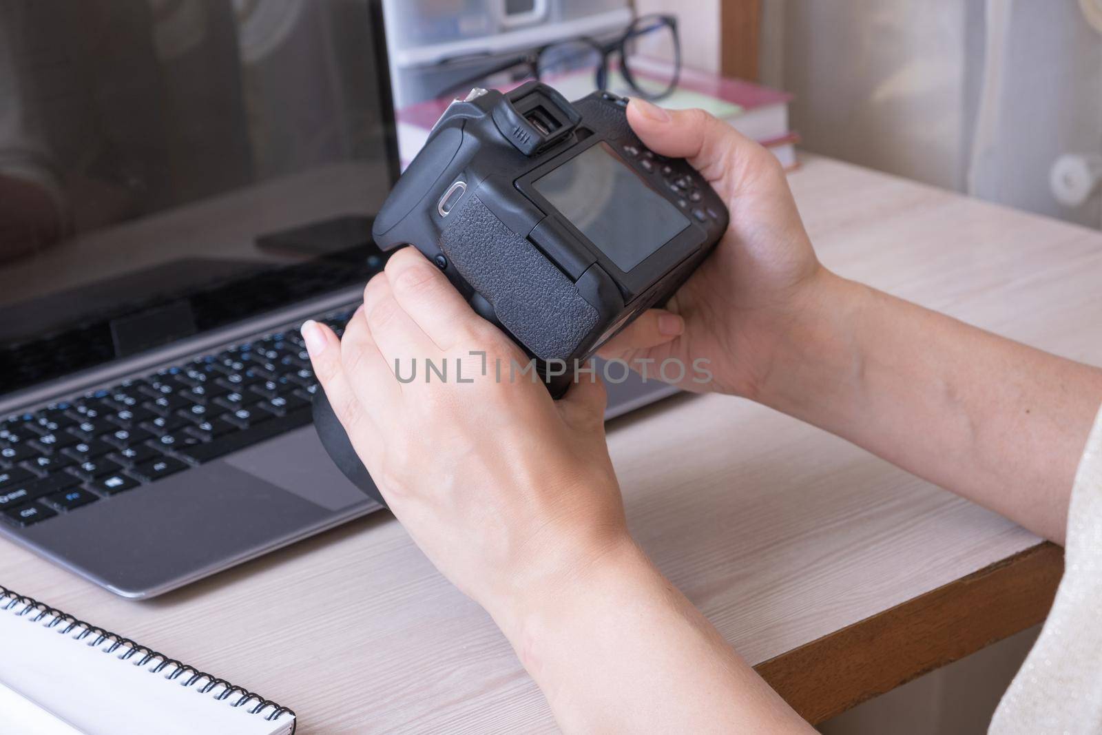 Studying online photography lessons. Female hands holding SLR camera at desktop with laptop.