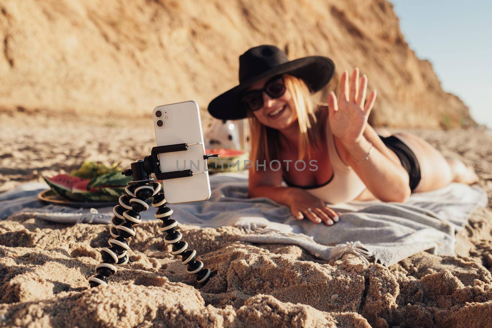 Smartphone Attached on Tripod in Focus, Young Woman Filming Herself on Mobile Camera While Enjoying Vacation by the Sea by Romvy
