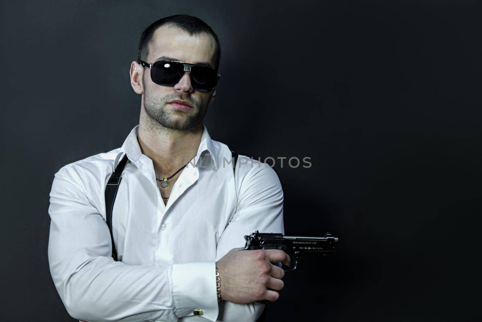 Young man in glasses wears a white shirt and suspenders, holds a gun in his hand