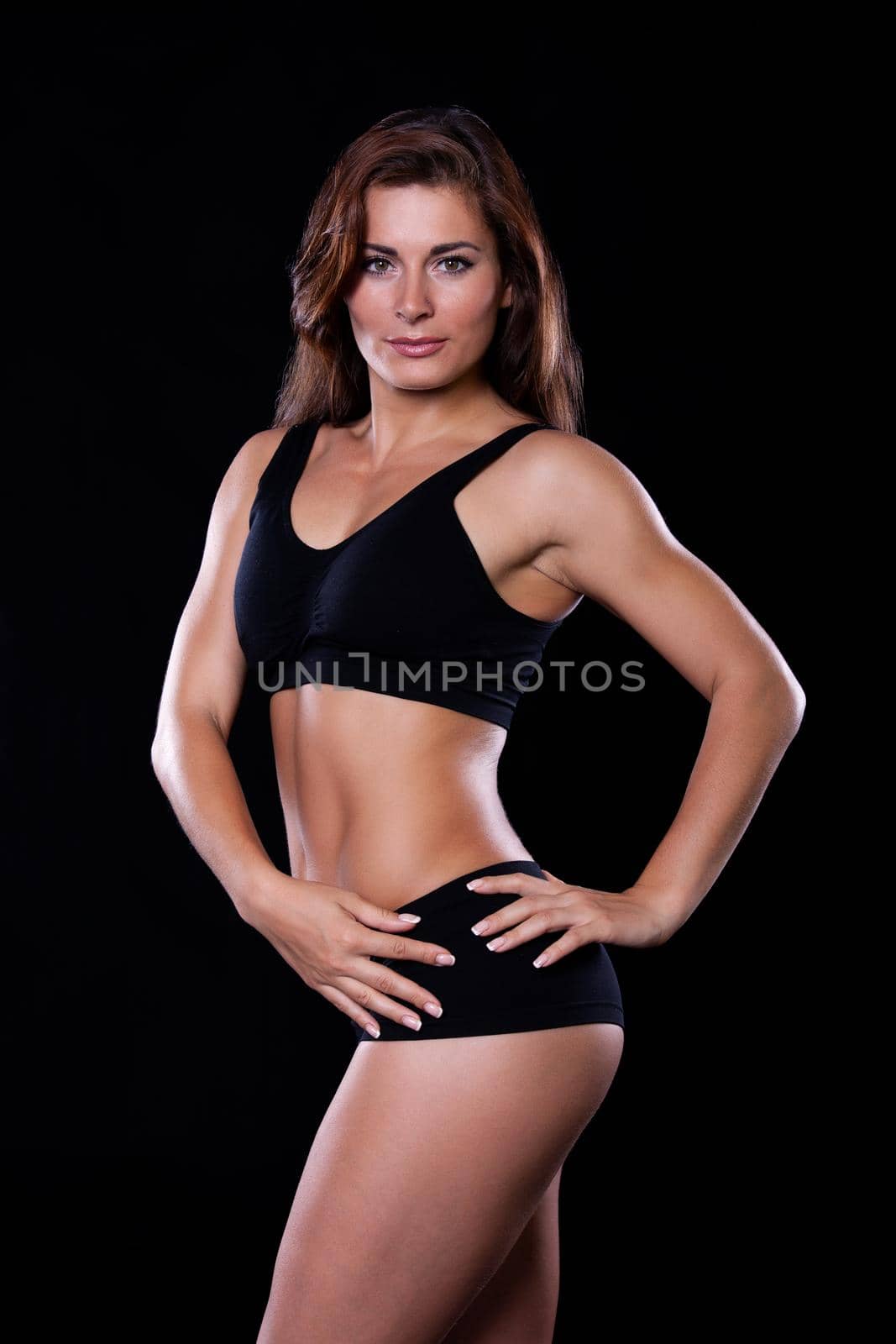 Sporty female brunette girl showing off her perfect body on black background
