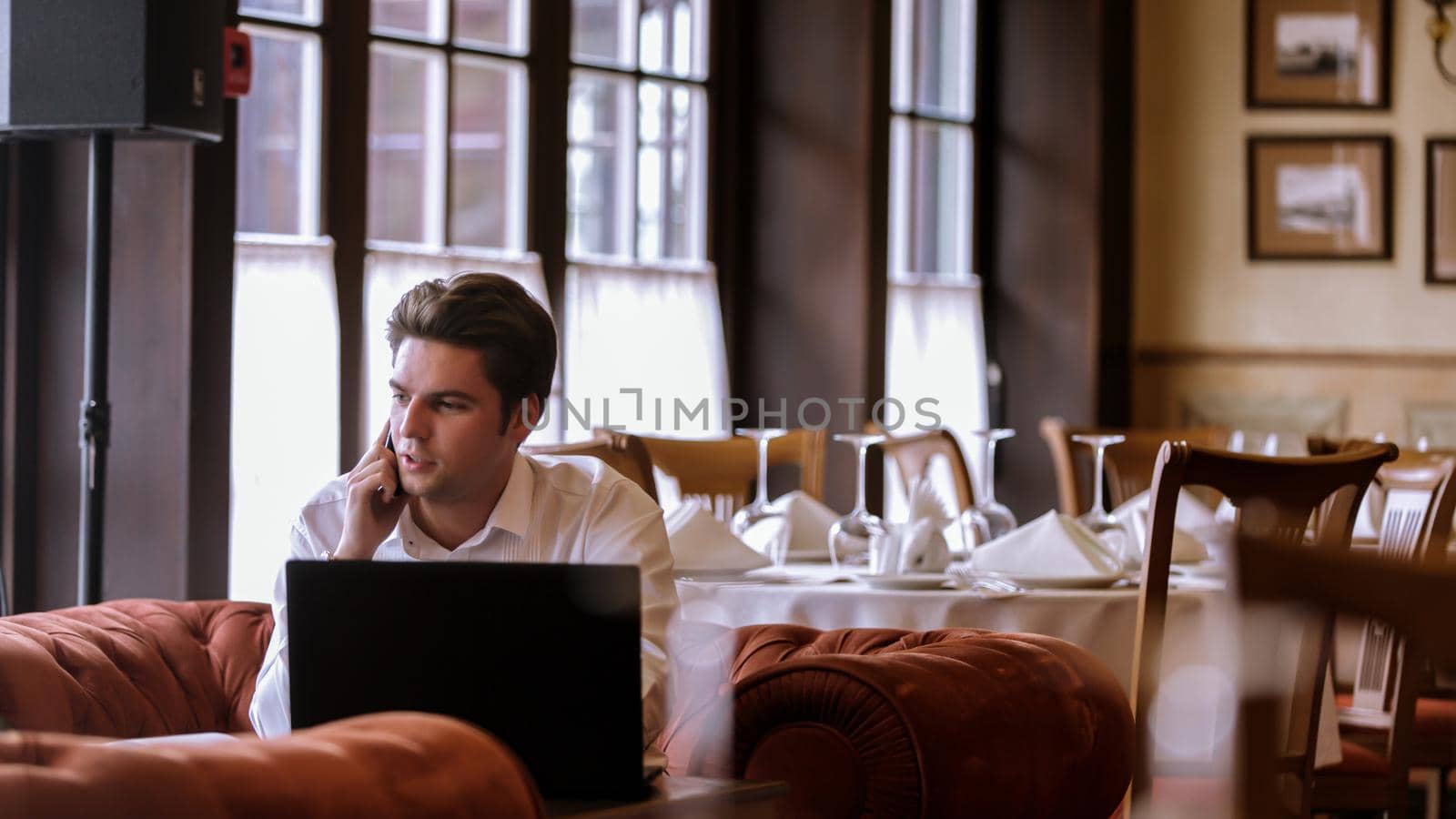 Portrait of goodlooking man sitting at table at home with laptop computer talking on the phone