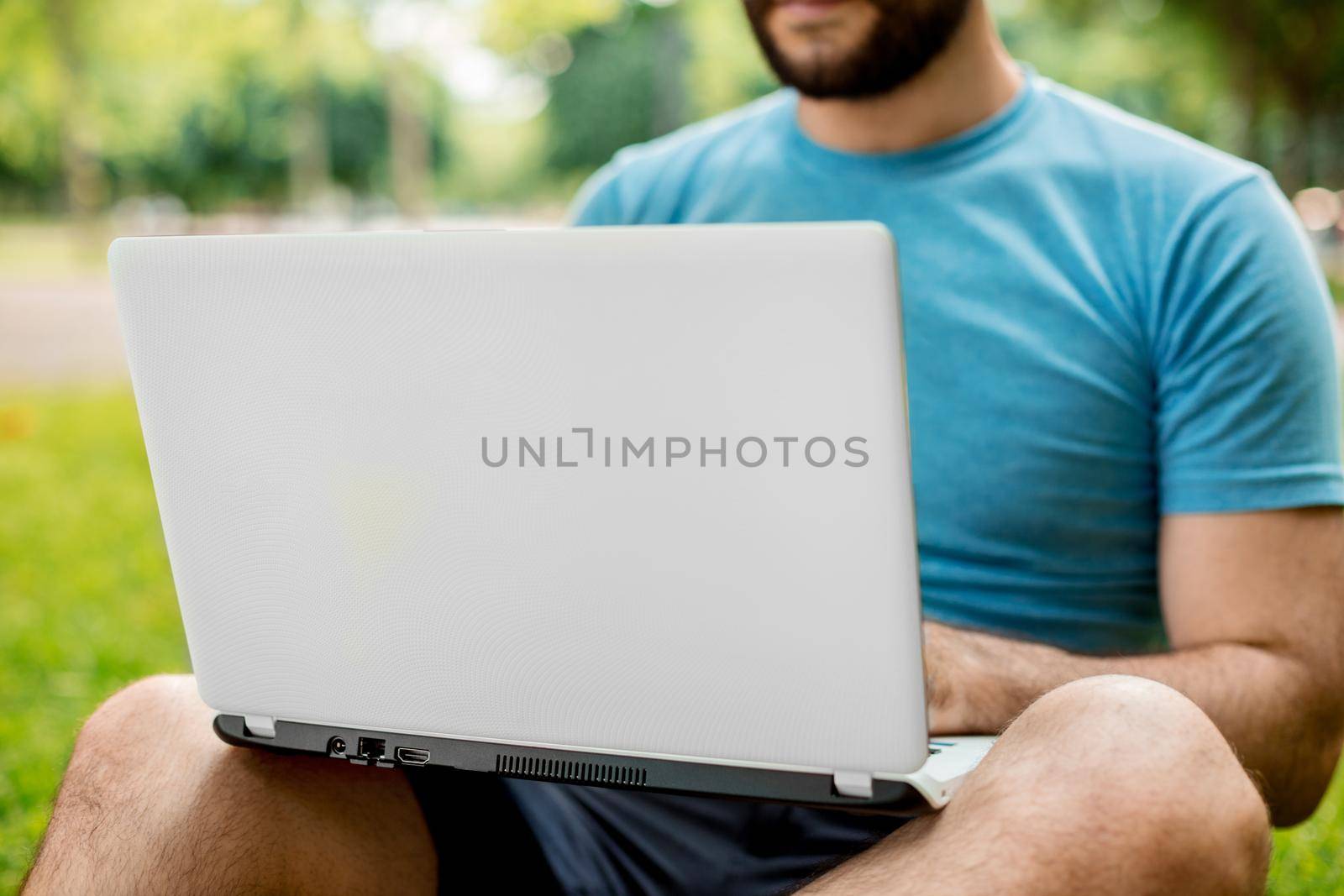 Young man using and typing laptop computer in summer grass. by nazarovsergey