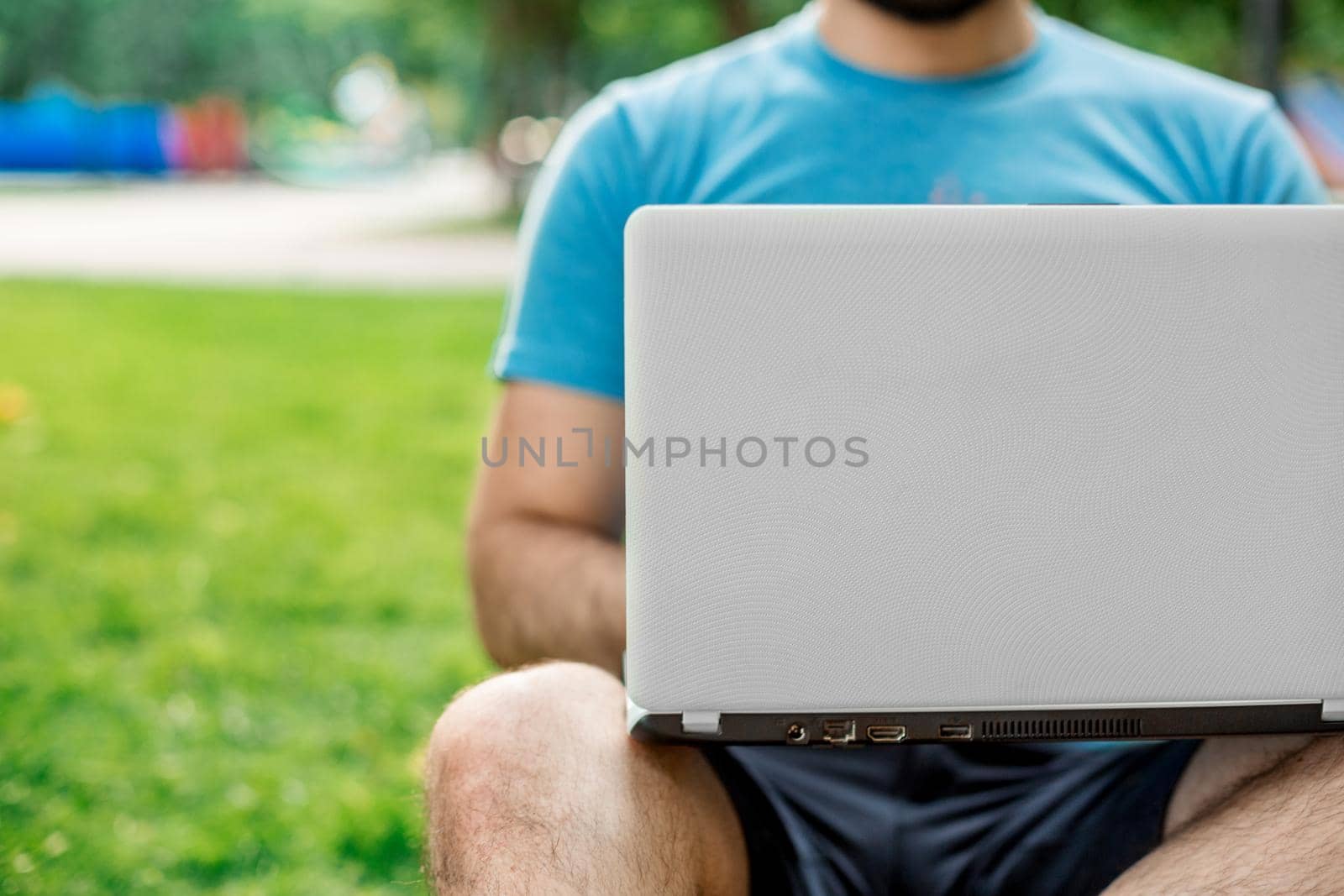 Young man using and typing laptop computer in summer grass. by nazarovsergey