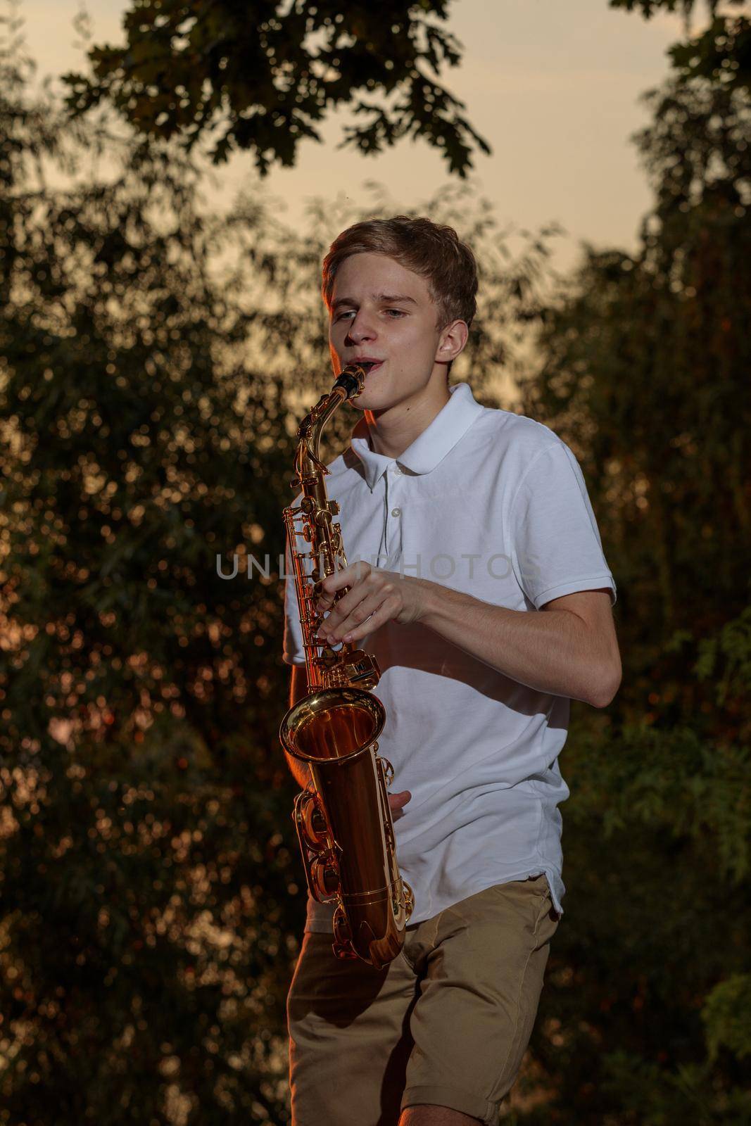 A young guy plays the saxophone in the evening at sunset.