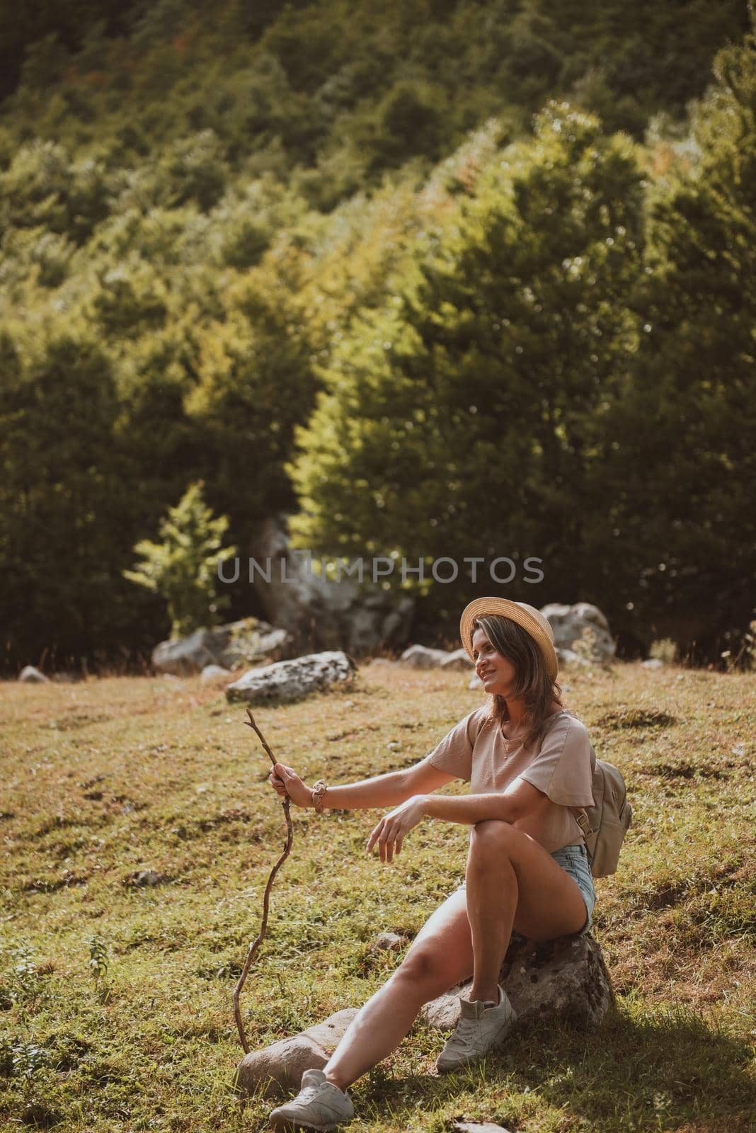 Travel, Lifestyle Concept. Beautiful woman enjoys views of the alpine village in the Alps mountains. Young woman sitting and relaxing on alpine mountain looking the cow eating a grass in the summer. Happy tourist girl traveling to Europe.