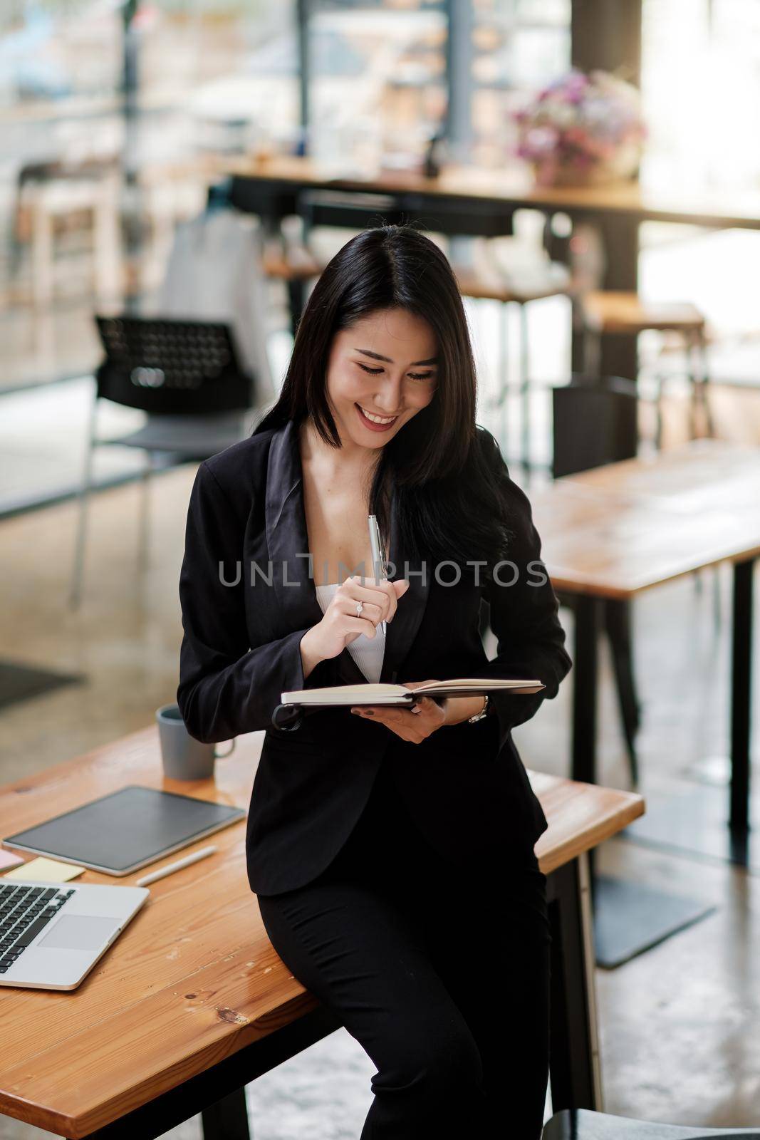 Portrait asian business woman working at office and taking note, Female sitting on desk and using laptop, tablet by nateemee