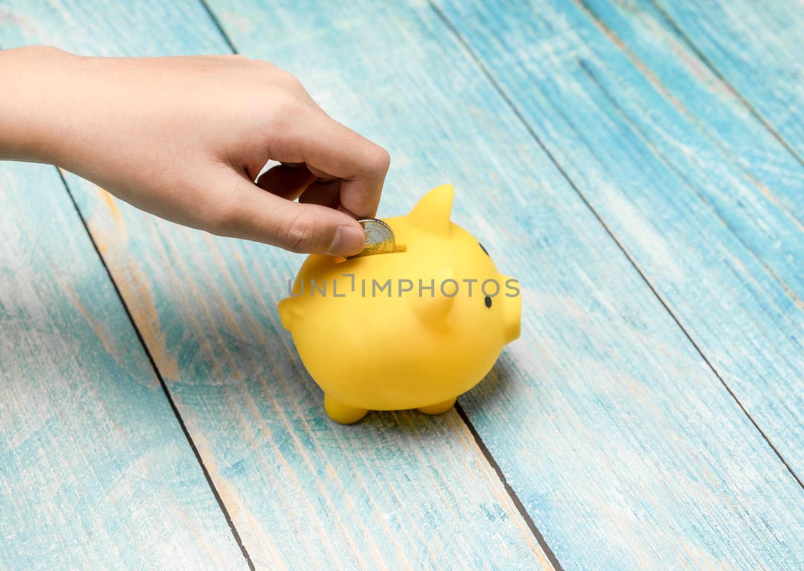 Hand putting money coin in yellow piggy bank for save and financial concept