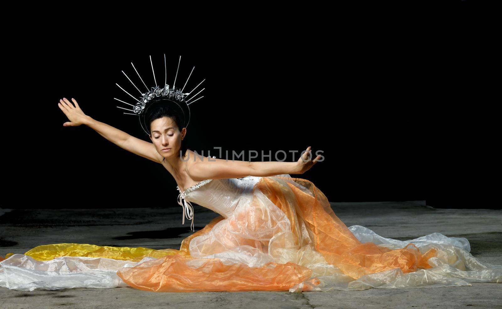 a beautiful woman of Caucasian appearance dressed in a chiffon skirt and a white corset with a crown on her head sits with her arms outstretched. Dance on a black background