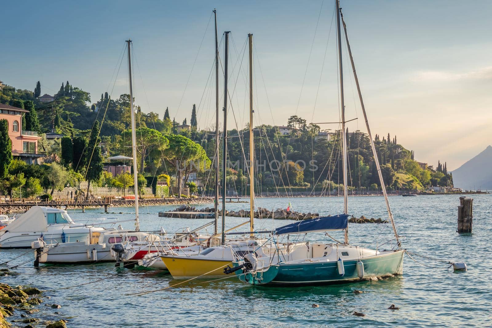 Idyllic lake Garda coastline and mediterranean village of Torbole with sailboats and mountains, Northern Italy