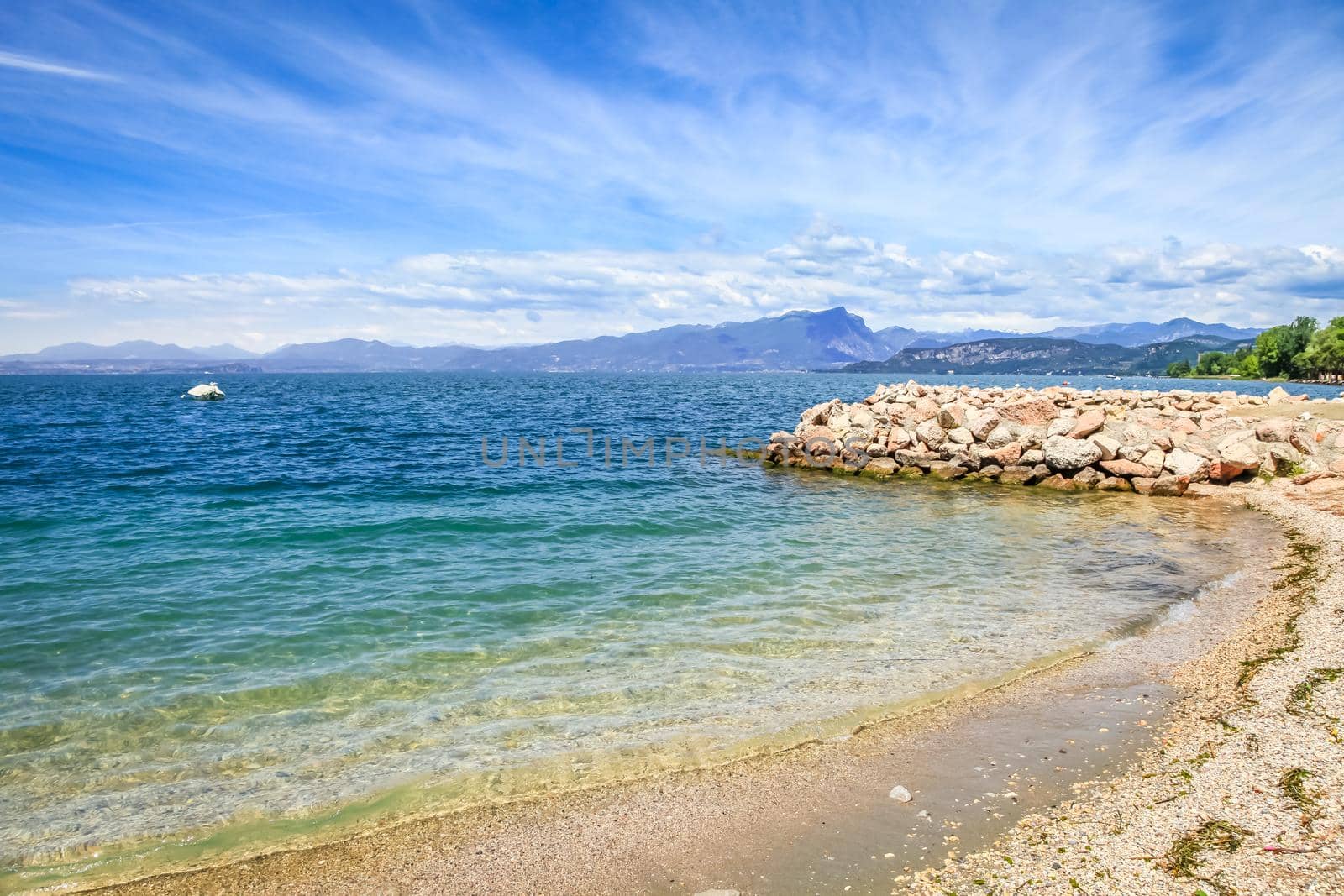 Idyllic lake Garda coastline in Lazise with boat and mountains, Northern Italy