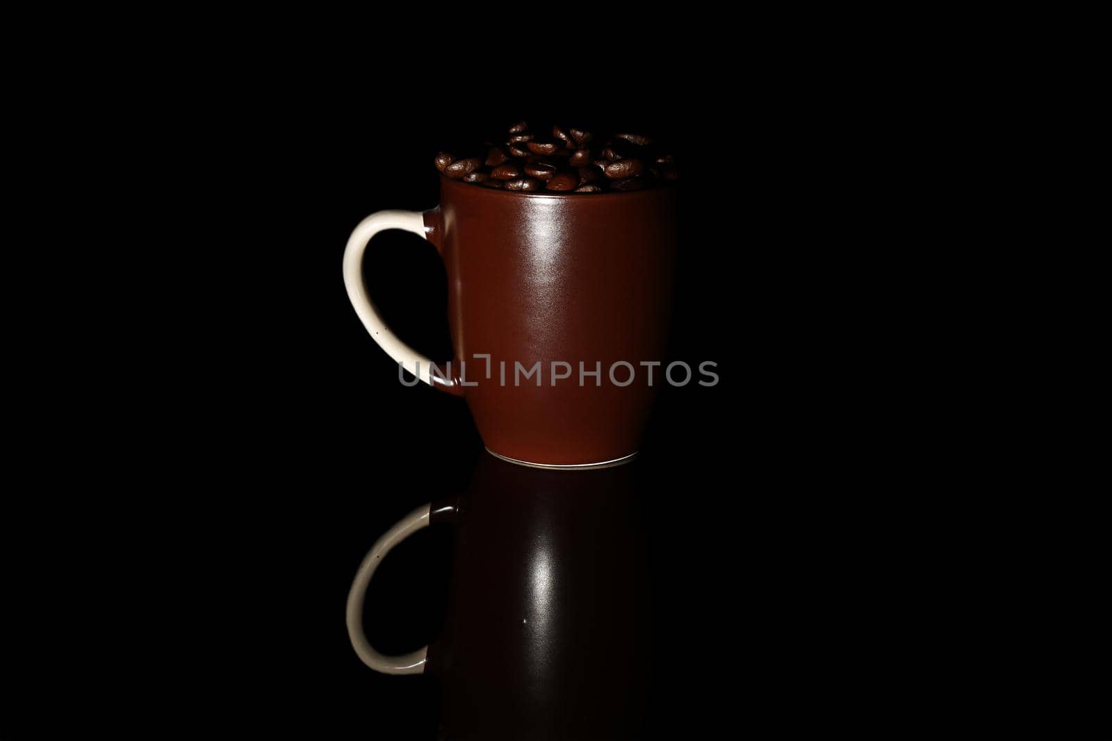 Coffee beans lie in dark brown mugs, on a black background. Isolated. Roasted coffee seeds. Close-up.
