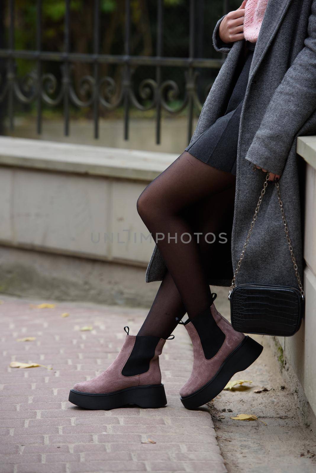 young beautiful girl posing on the autumn street. Dressed in a stylish gray coat, knitted pink sweater and skirt.