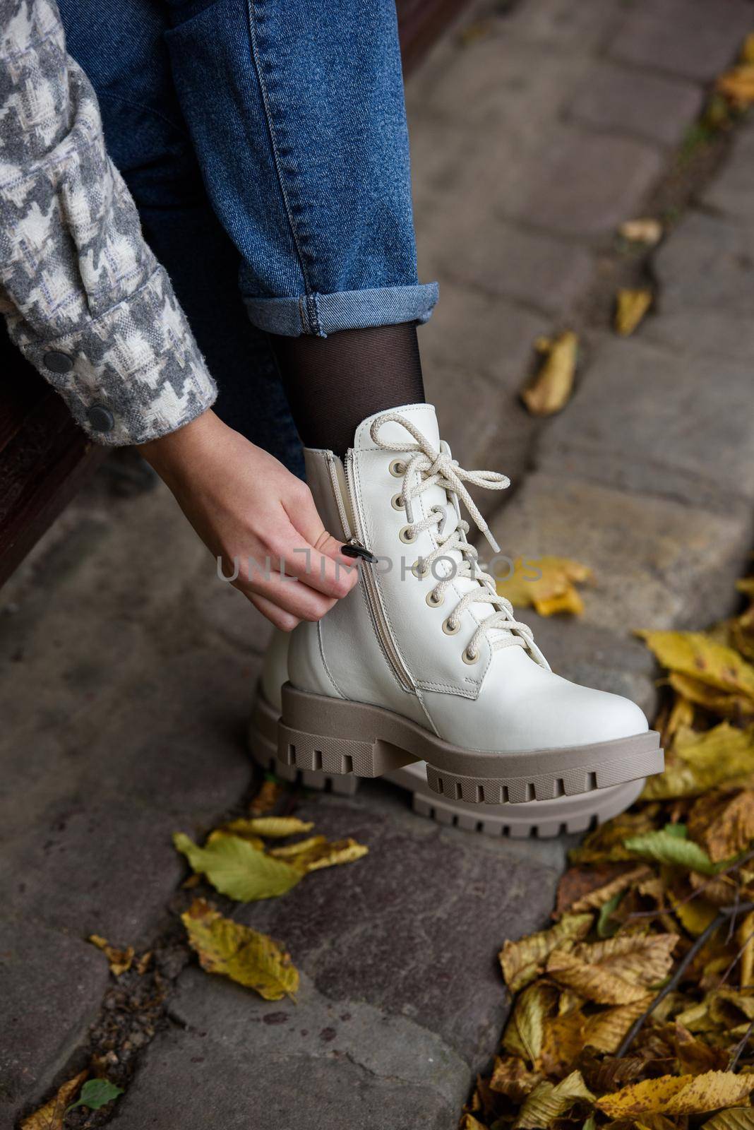 Female legs in a jeans and white fashion boots with laces. fallen leaves on the sidewalk