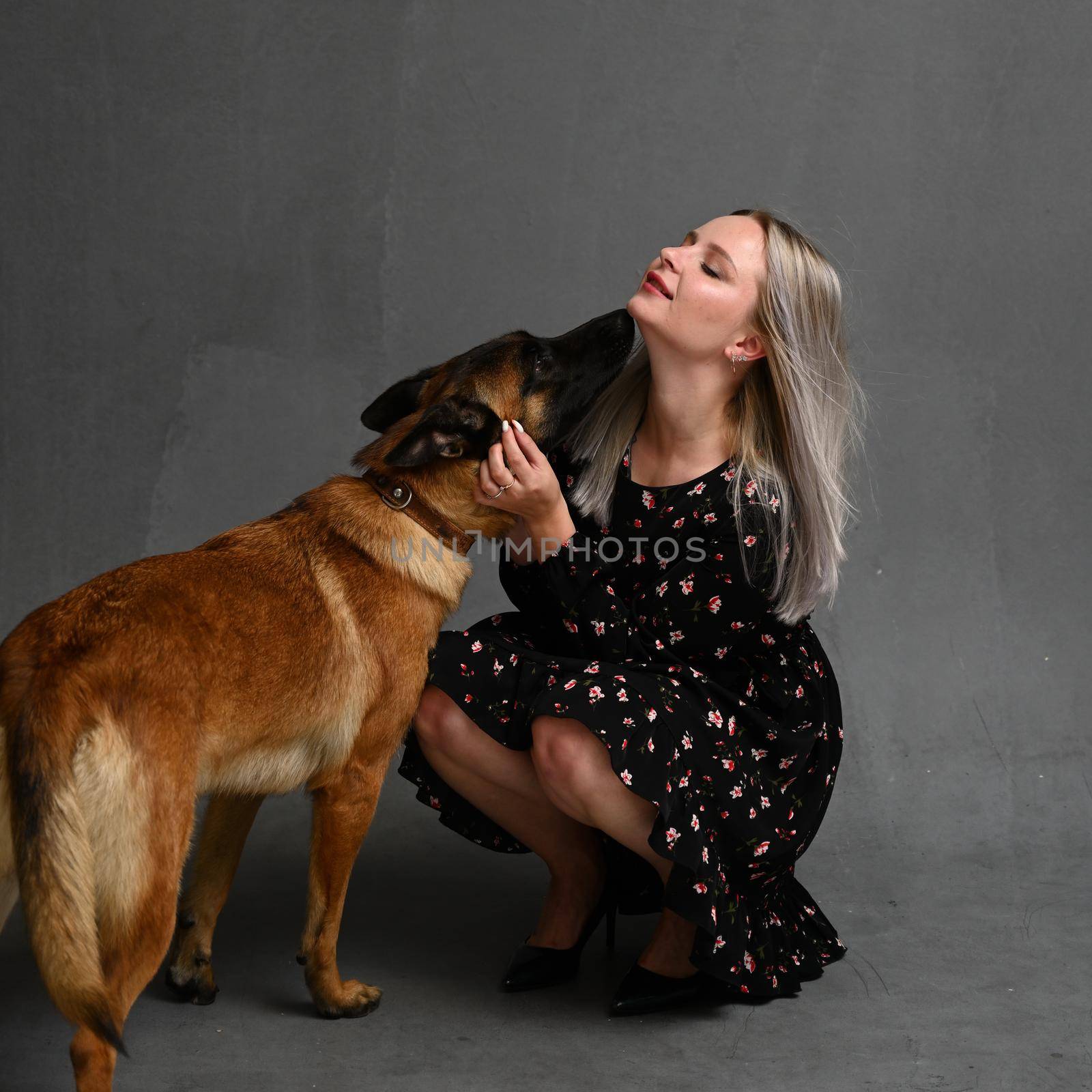 Adult girl carries dog which embraces her around neck walk together isolated over gray background. Female dog lover poses with pet looks away likes animals. Care and love