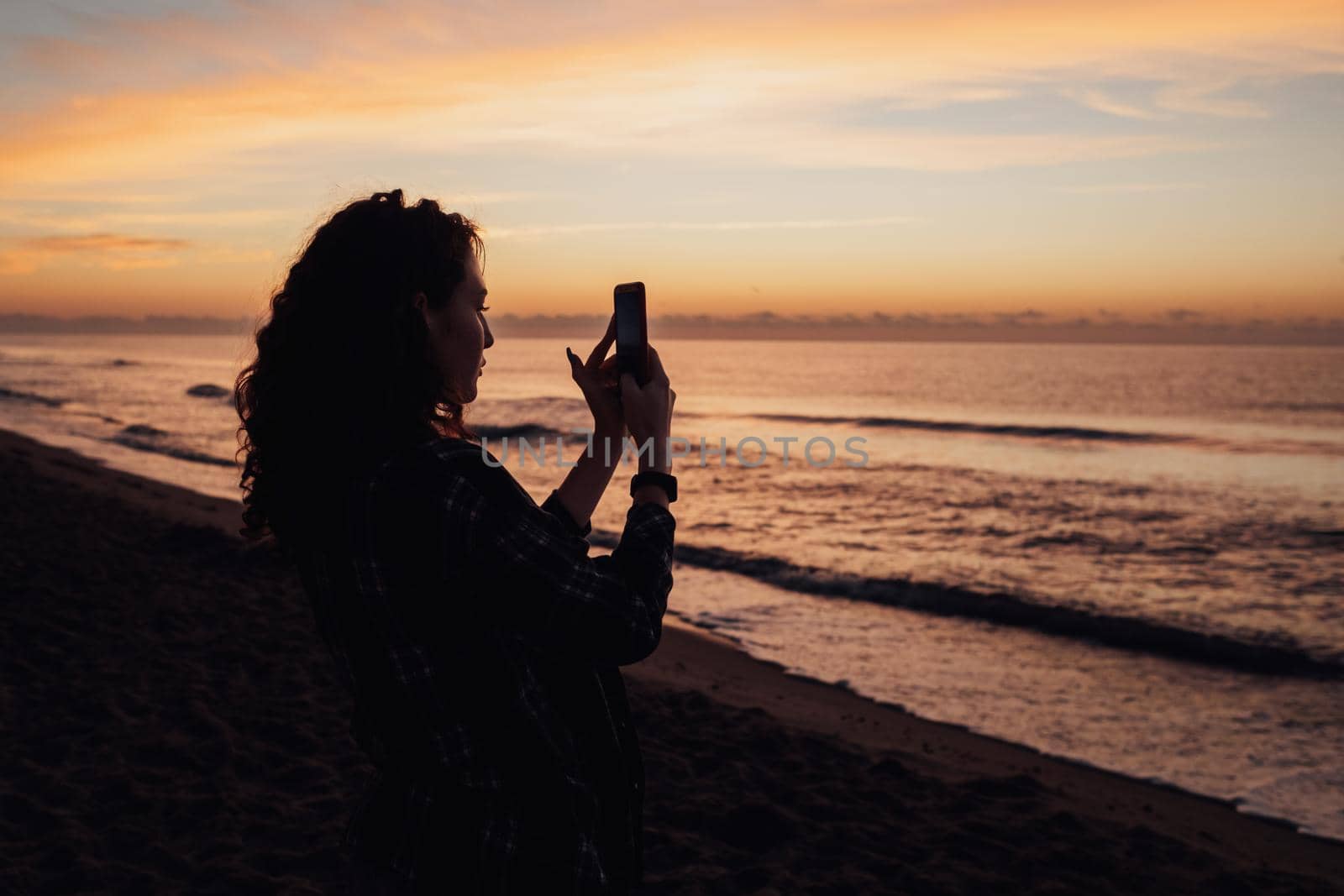 Woman meets the dawn and takes pictures of the sea on smartphone with scenic landscape on the background