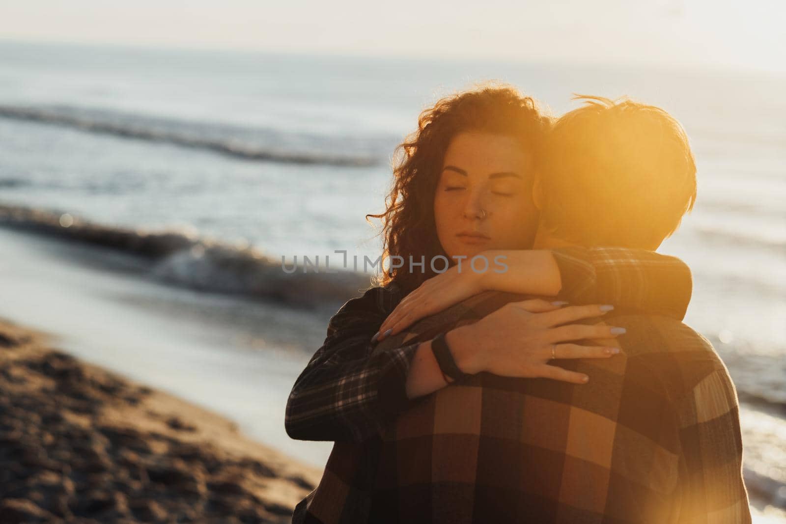 Young woman and man, sweet couple hugging together against the background of sea and the sun's rays at dawn