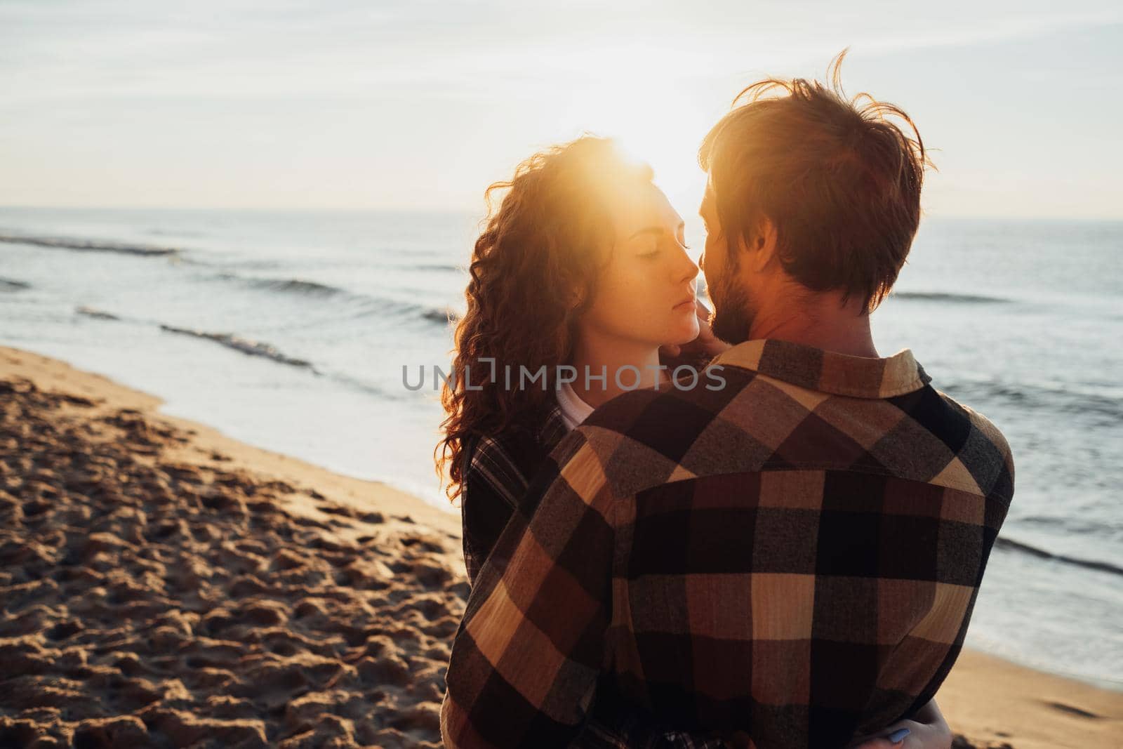 Young woman and man hugging together and come for a kiss against the background of sea and the sun's rays at dawn