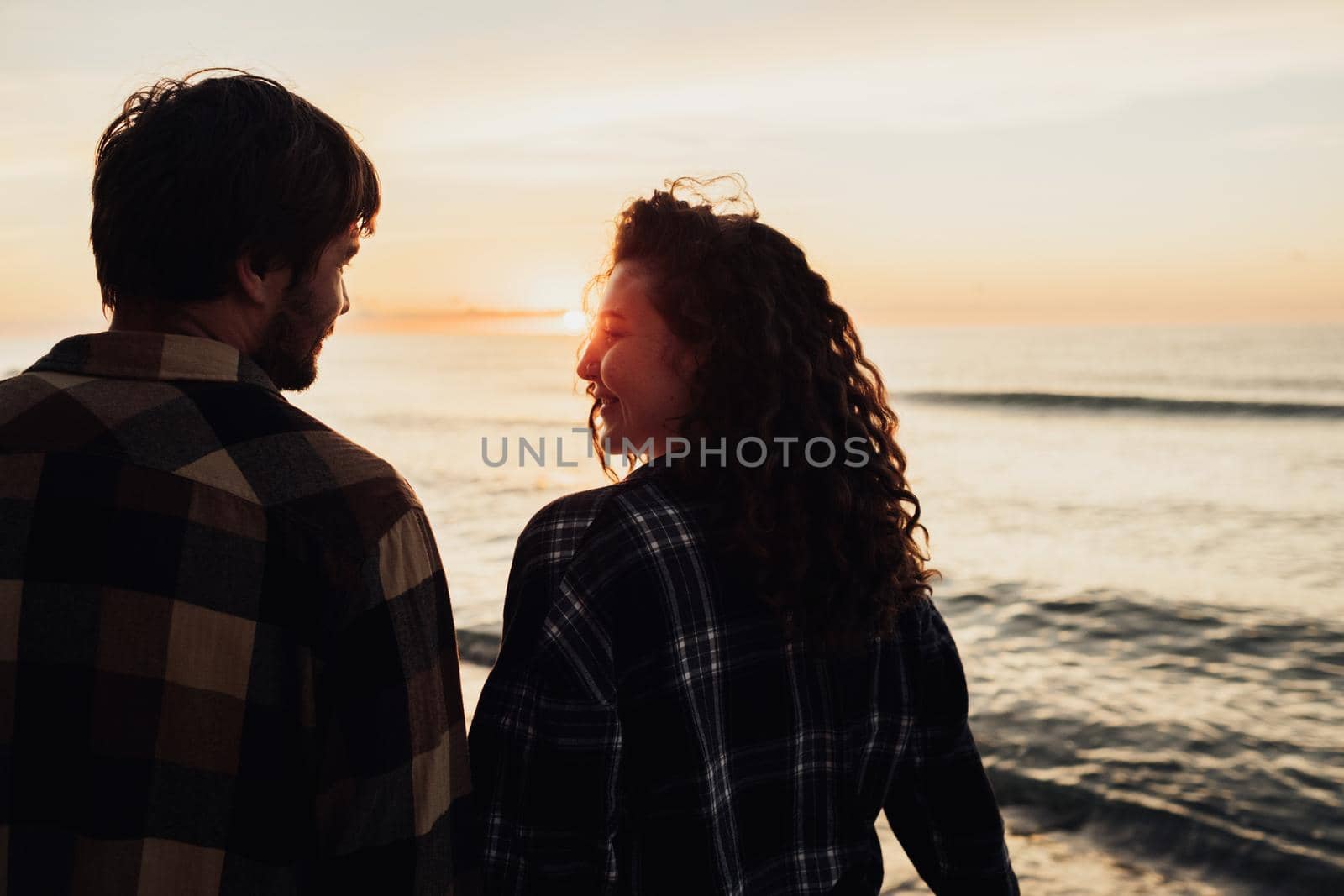 Woman and man holding hands together and walking along sea coast at dawn, young couple meeting sunrise together