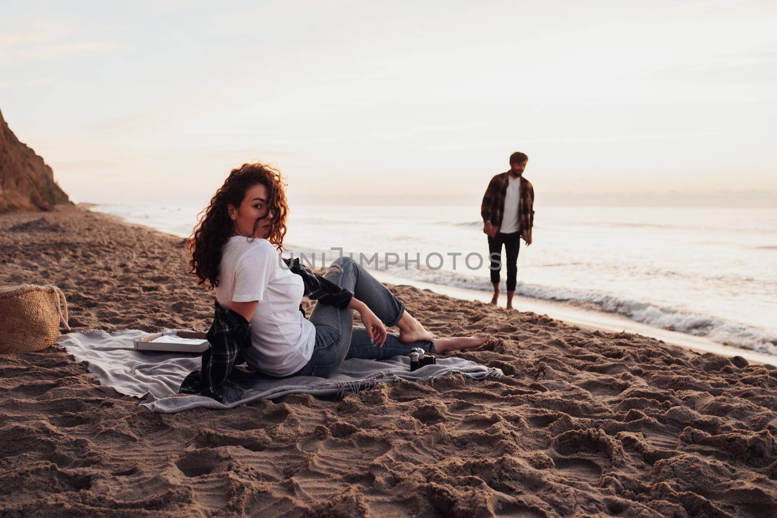 Young couple having picnic on beach at dawn, woman and man meeting sunrise together on the sea