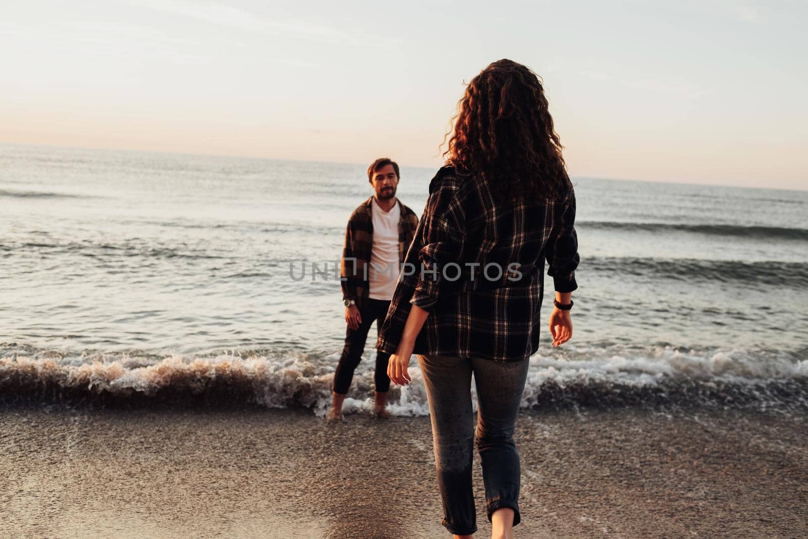Woman coming to boyfriend that standing in the water on the seashore, young couple meeting sunrise on sea together.