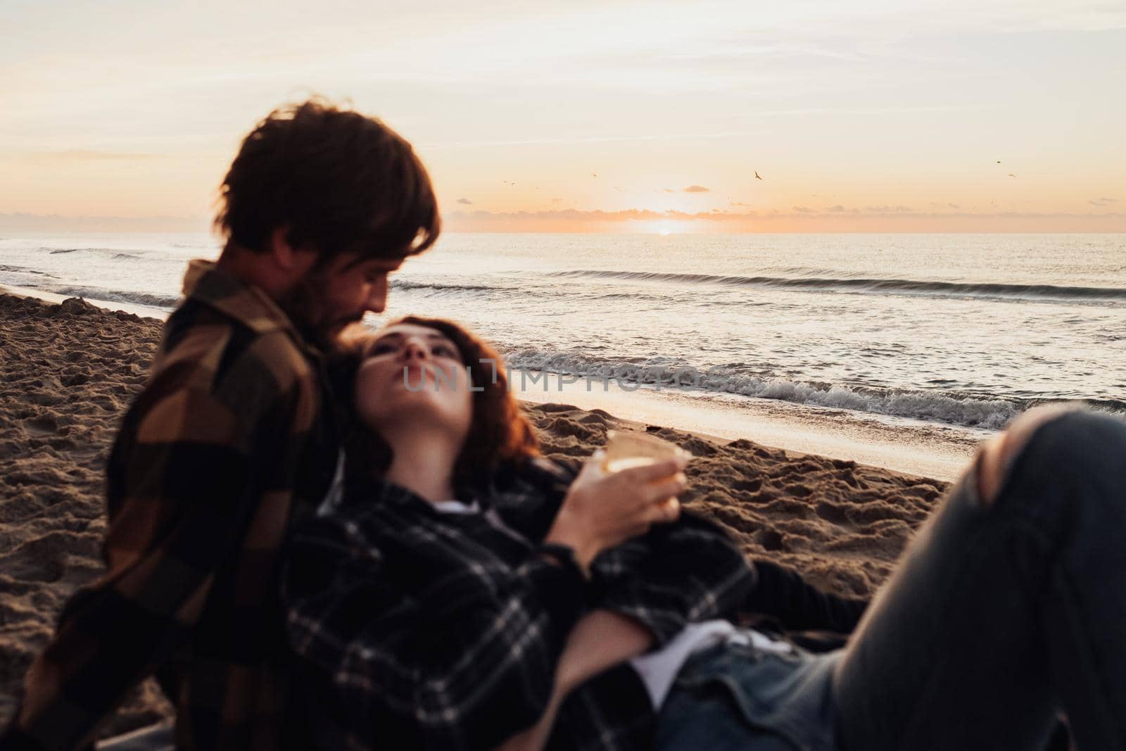 Focus on the sea horizon, young couple meeting sunrise together, woman and man lying on beach at dawn