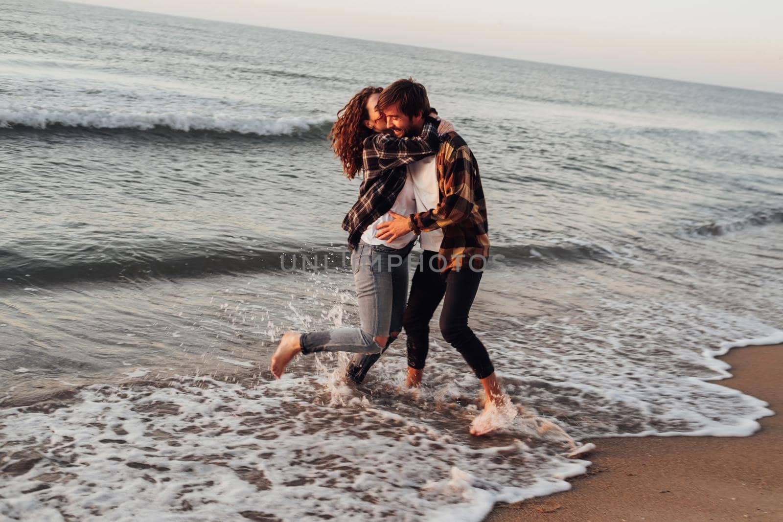 Young woman and man hugging and kissing together while standing on seashore at dawn