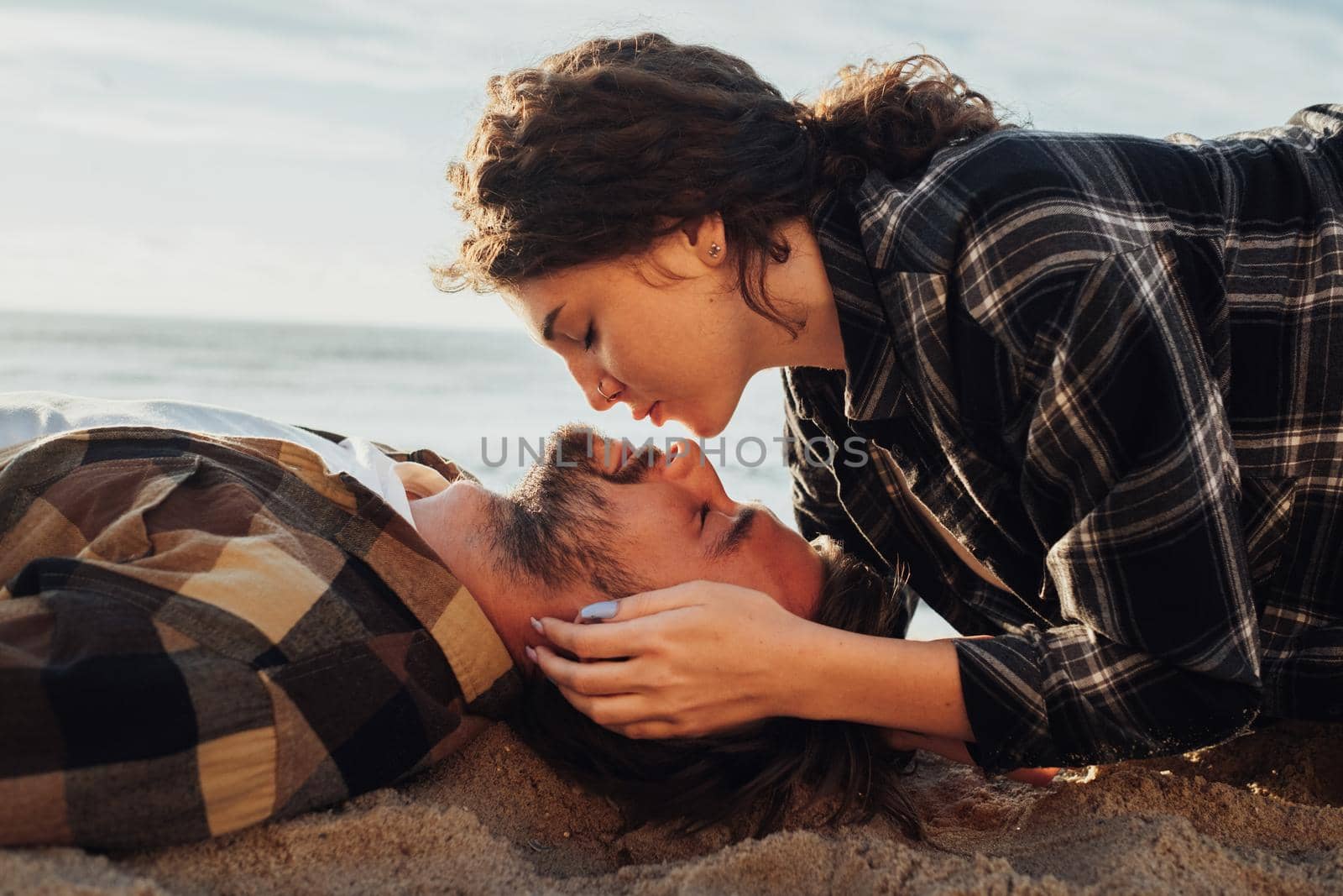 Young adult couple laying on the beach of sea, caucasian curly woman kissing her boyfriend by Romvy