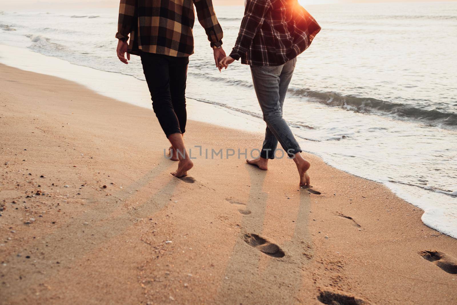Unrecognisable couple meeting sunrise on seashore, man and woman holding by hands walking along the coastline