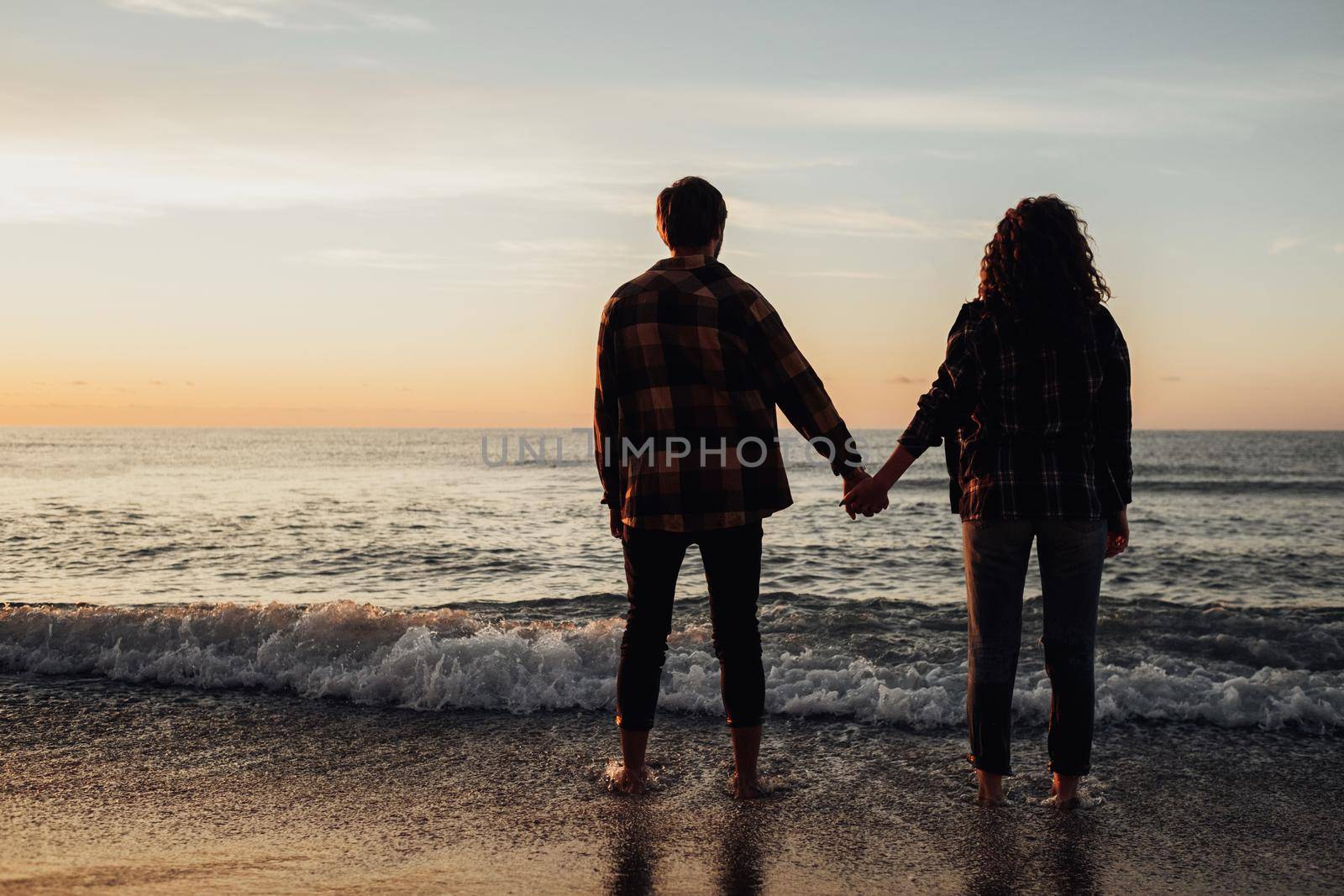 Young couple meeting sunrise on seashore, man and woman holding by hands standing in water