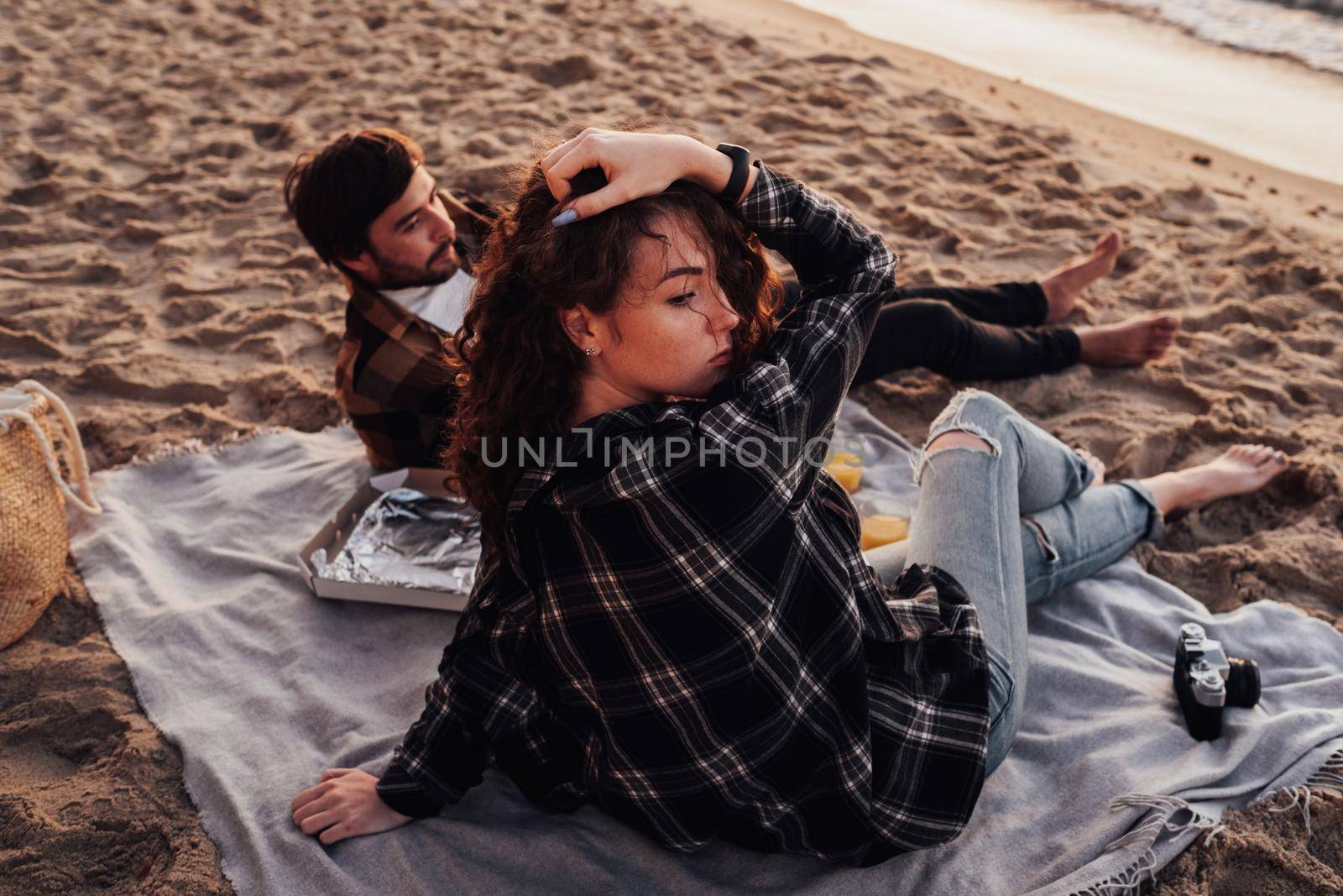 Young couple having picnic on beach at dawn, woman and man meeting sunrise together on the sea