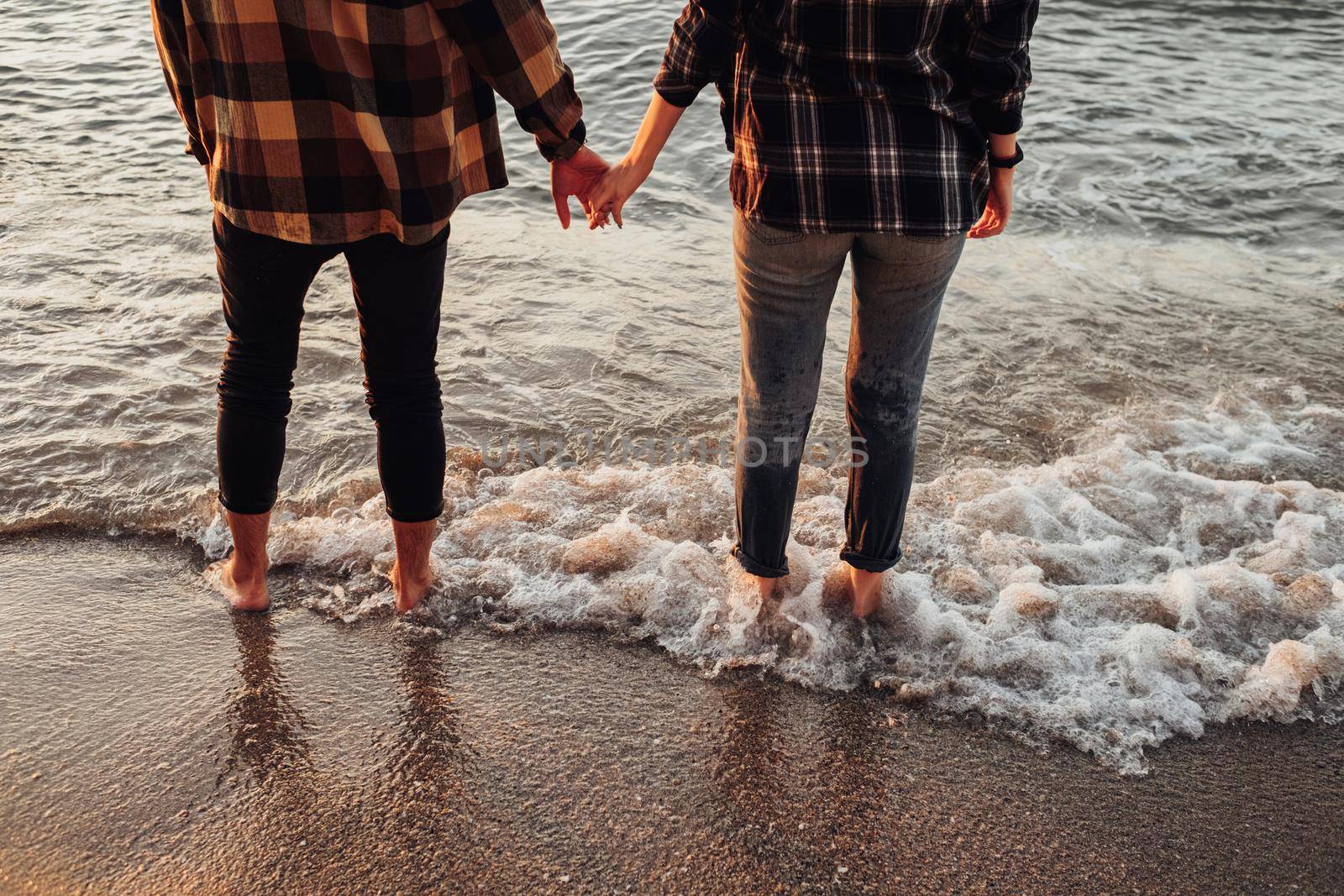 Unrecognisable couple meeting sunrise on seashore, man and woman holding by hands standing in water