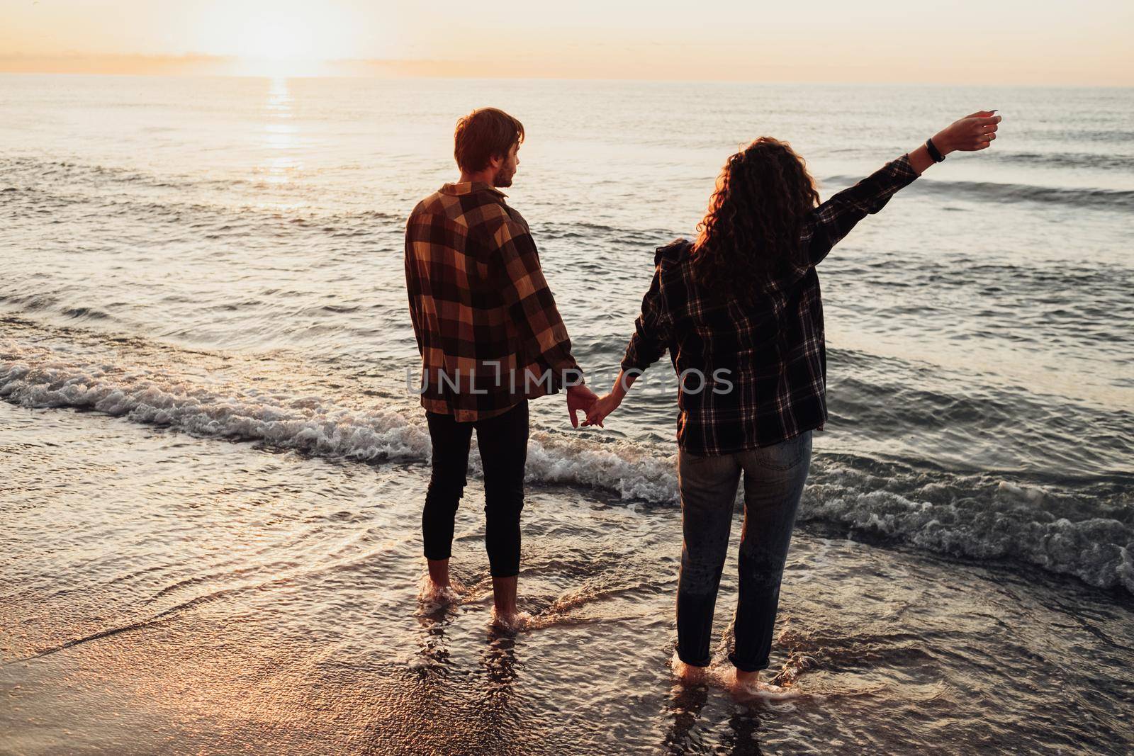 Young couple meeting sunrise on the seashore, man and woman holding by hands standing in water by Romvy