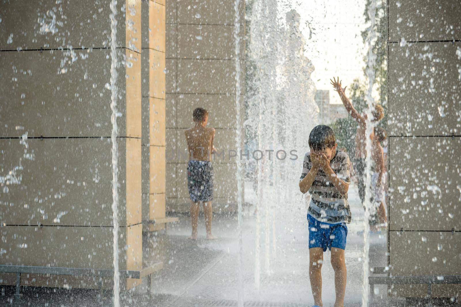 Boy having fun in water fountains. Child playing with a city fountain on hot summer day. Happy kids having fun in fountain. Summer weather. Active leisure, lifestyle and vacation.